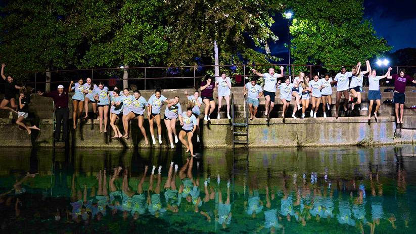 President Kelly Damphousse jumps in the river with the volleyball team and coaching staff.