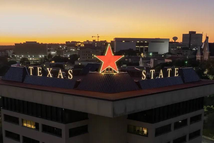 The Victory Star glows on top of the JC Kellam building. The star is maroon while the words "Texas State" are gold. 