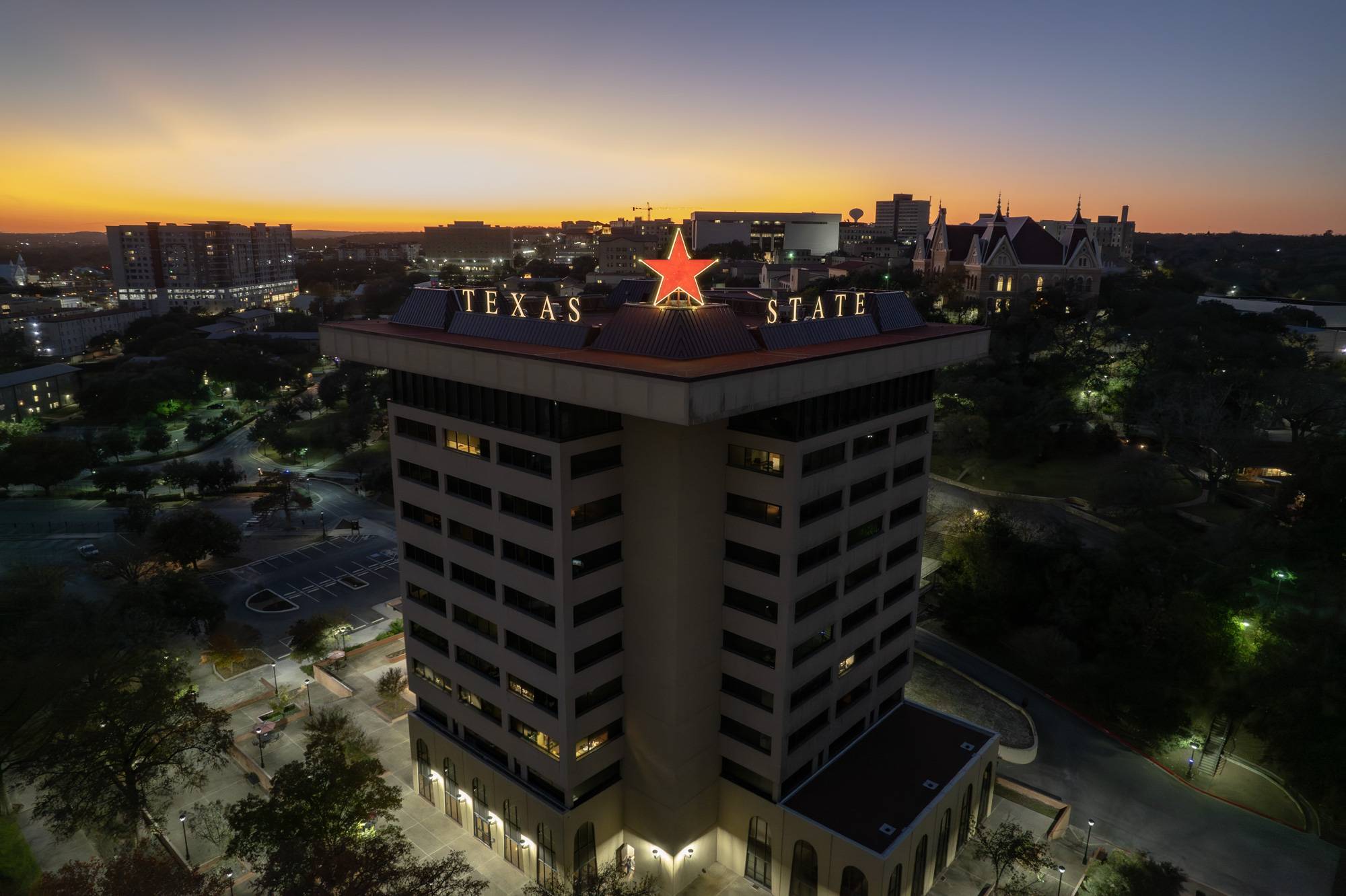 The Victory Star glows on top of the JC Kellam building. The star is maroon while the words "Texas State" are gold. 