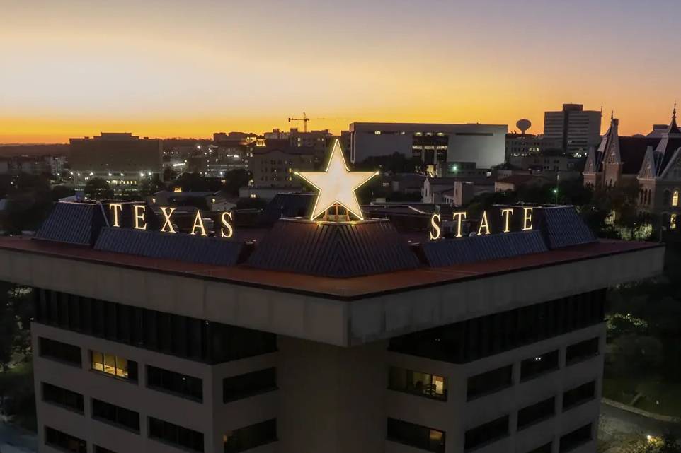 The Victory Star glows on top of the JC Kellam building. Both the star and "Texas State" are lit up in gold. 