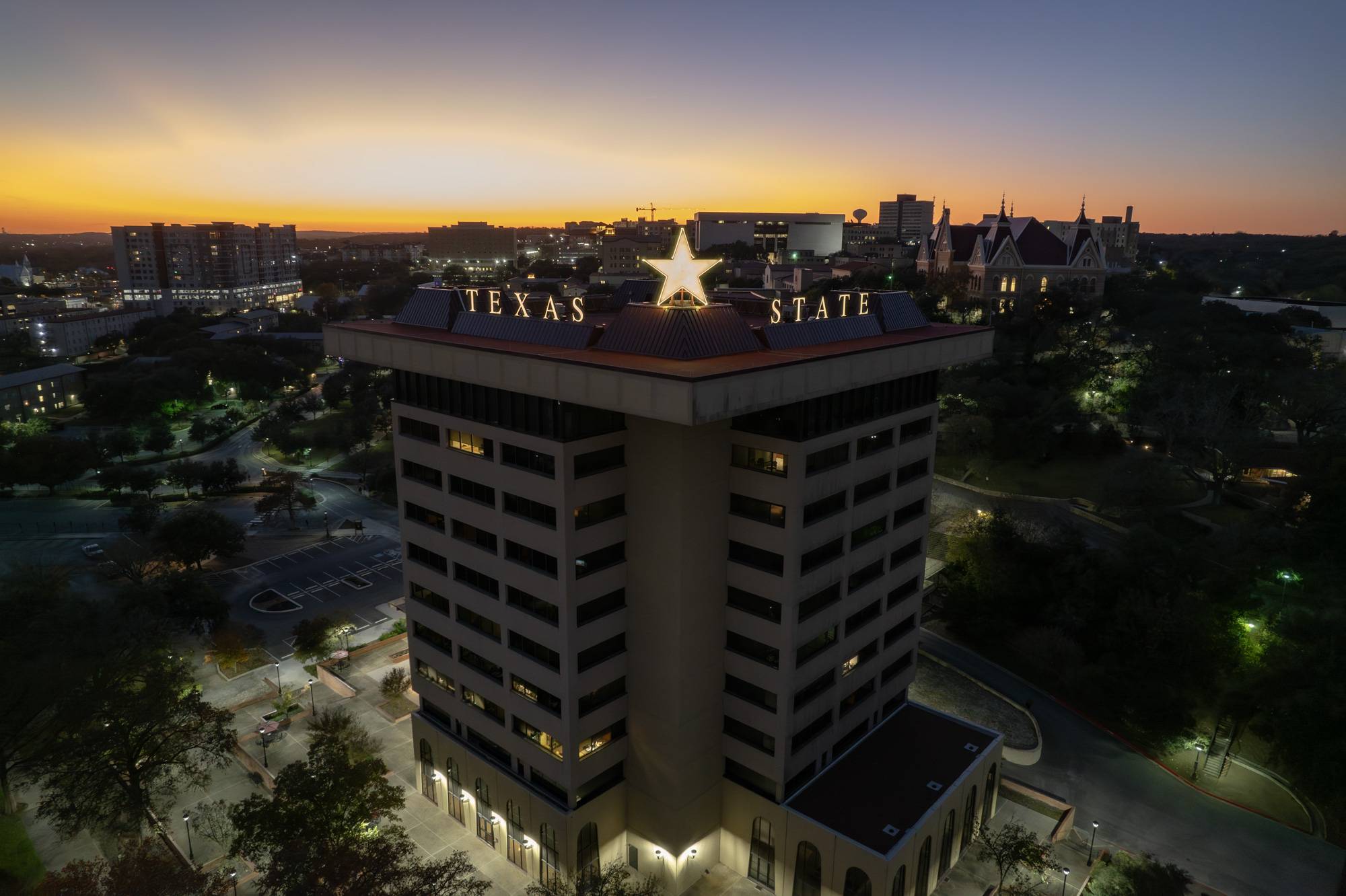 The Victory Star glows on top of the JC Kellam building. Both the star and "Texas State" are lit up in gold. 