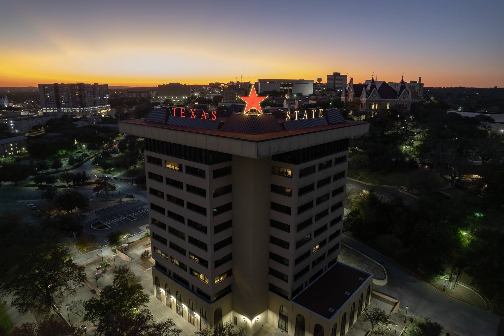 The Victory Star glows on top of the JC Kellam building.  Both the star and "Texas State" are lit up in maroon. 