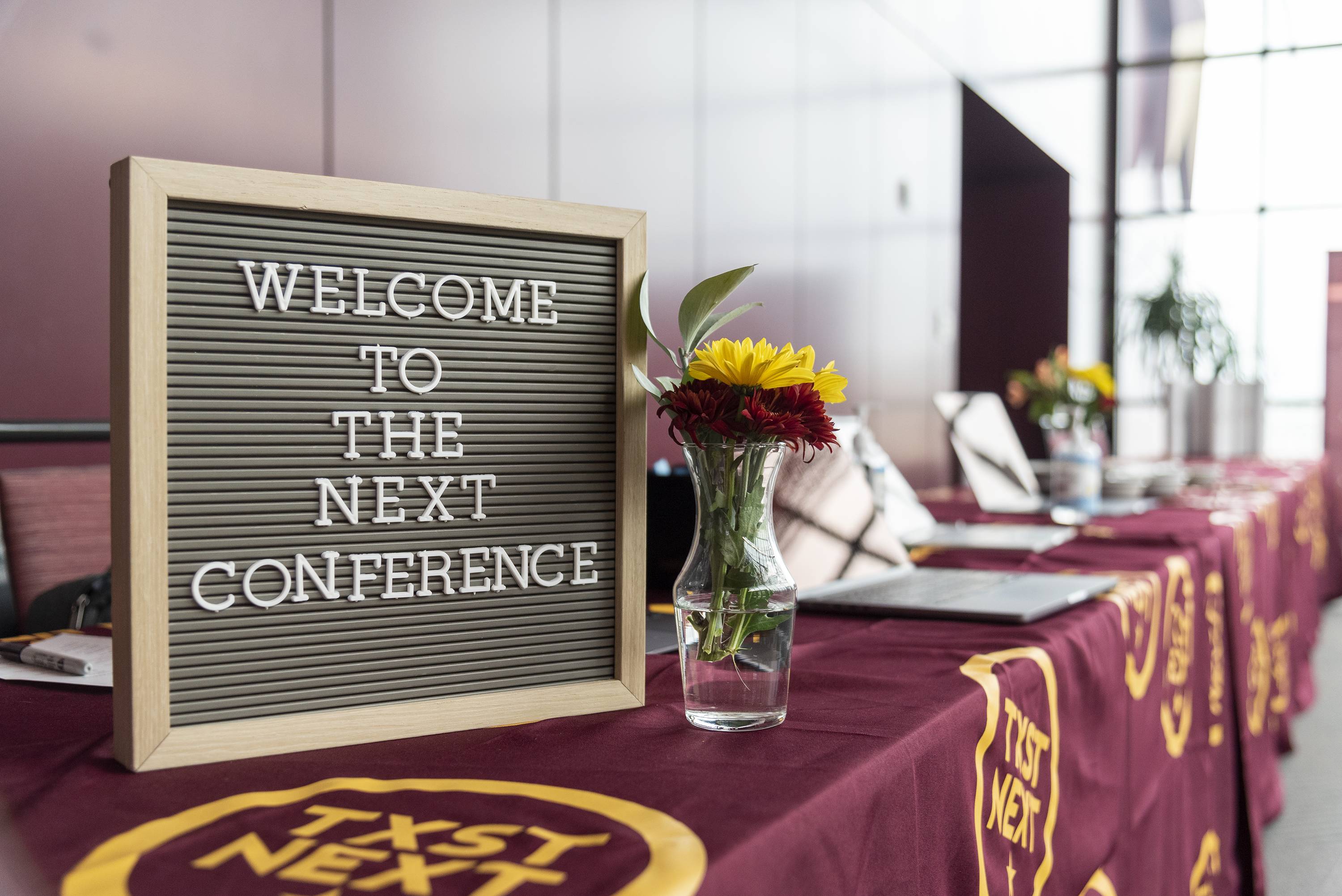 sign on a maroon tablecloth that welcomes you to the next conference