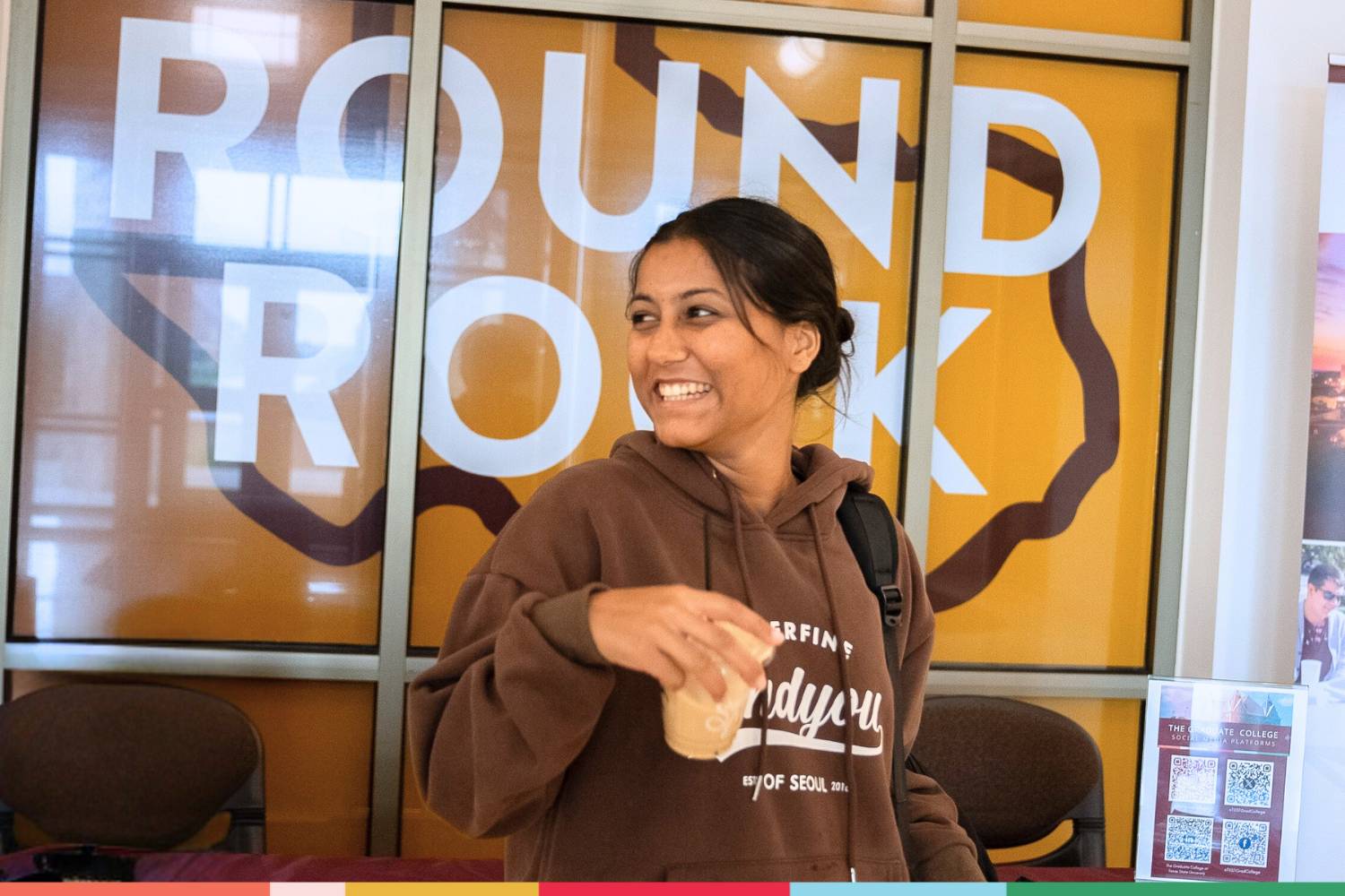 A student smiling while standing in front of a round rock sign