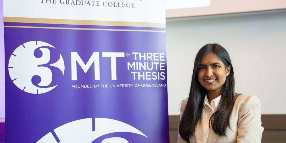 Anjumand Ashraf standing next to a 3MT sign holding her name tag and runner-up annoucement