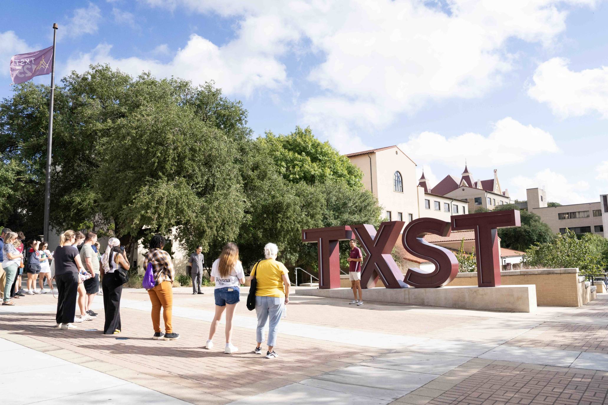 Prospective students and family gather around the TXST sign on San Marcos campus