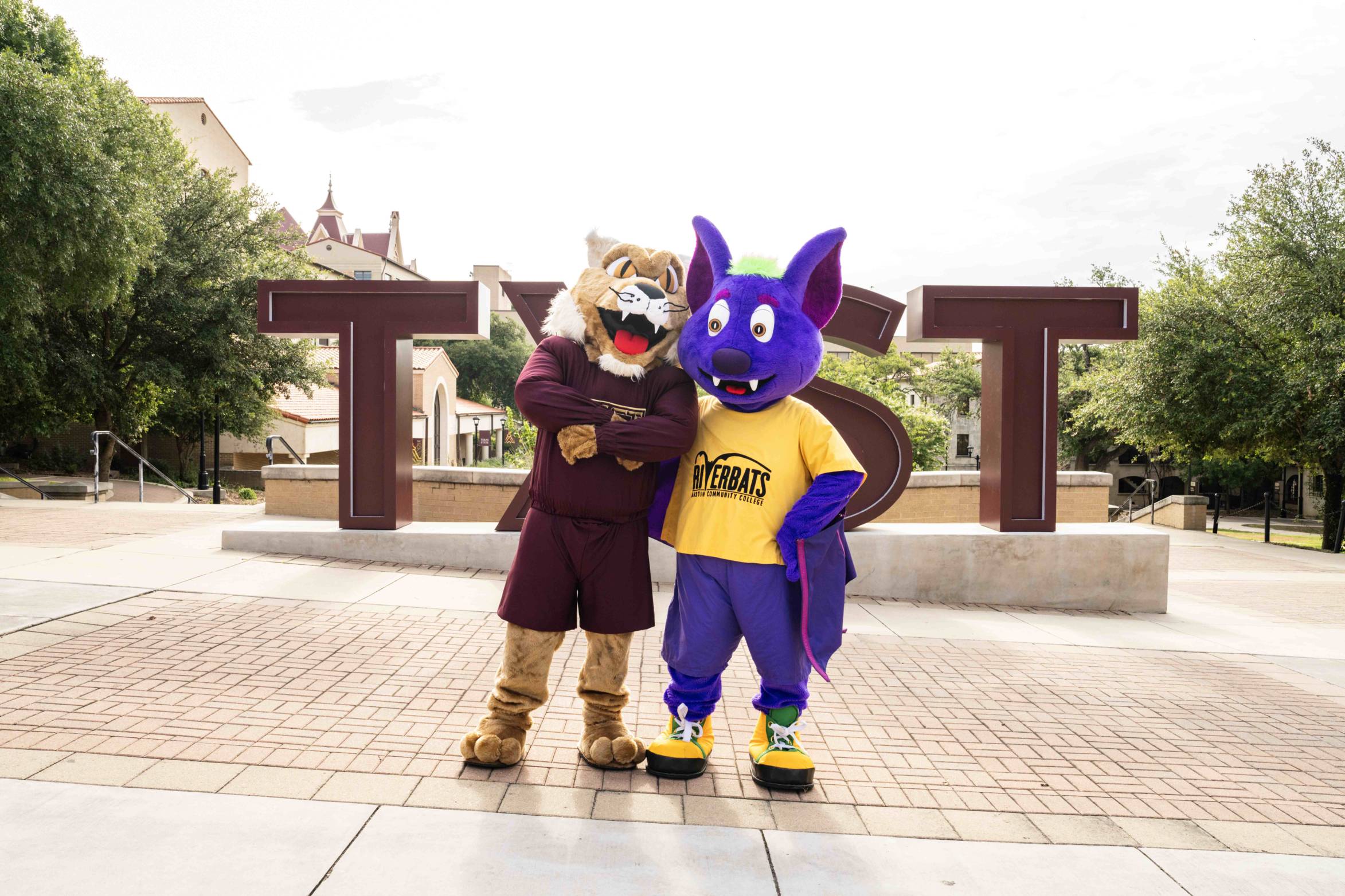 Boko the Bobcat and R.B. the Riverbat pose in front of the TXST sign.