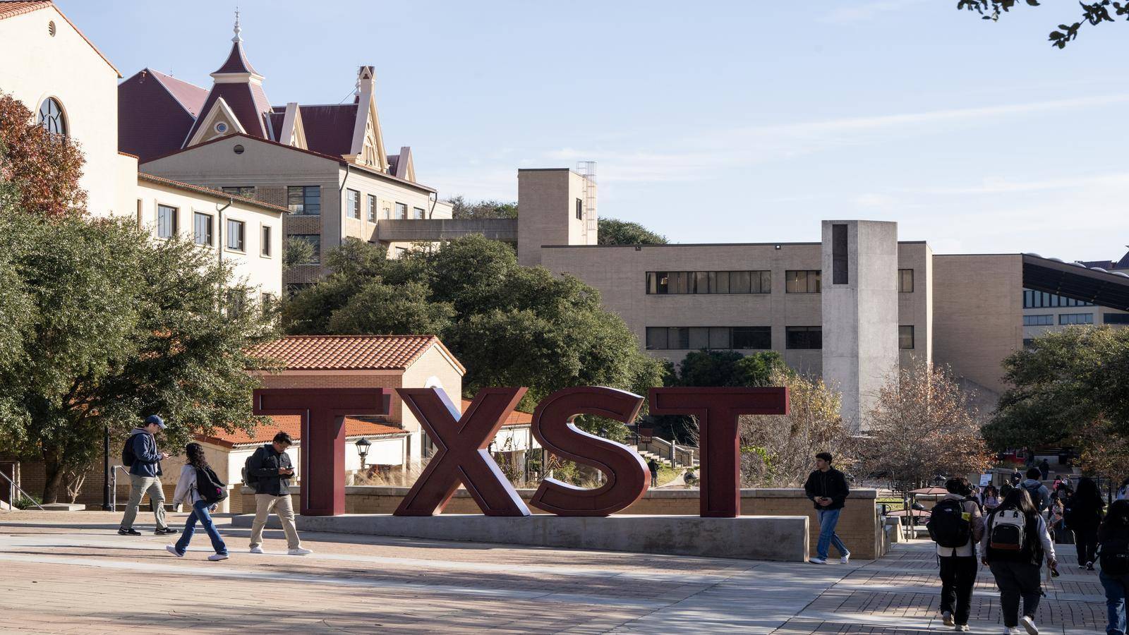 University students walk across campus in front of TXST sign