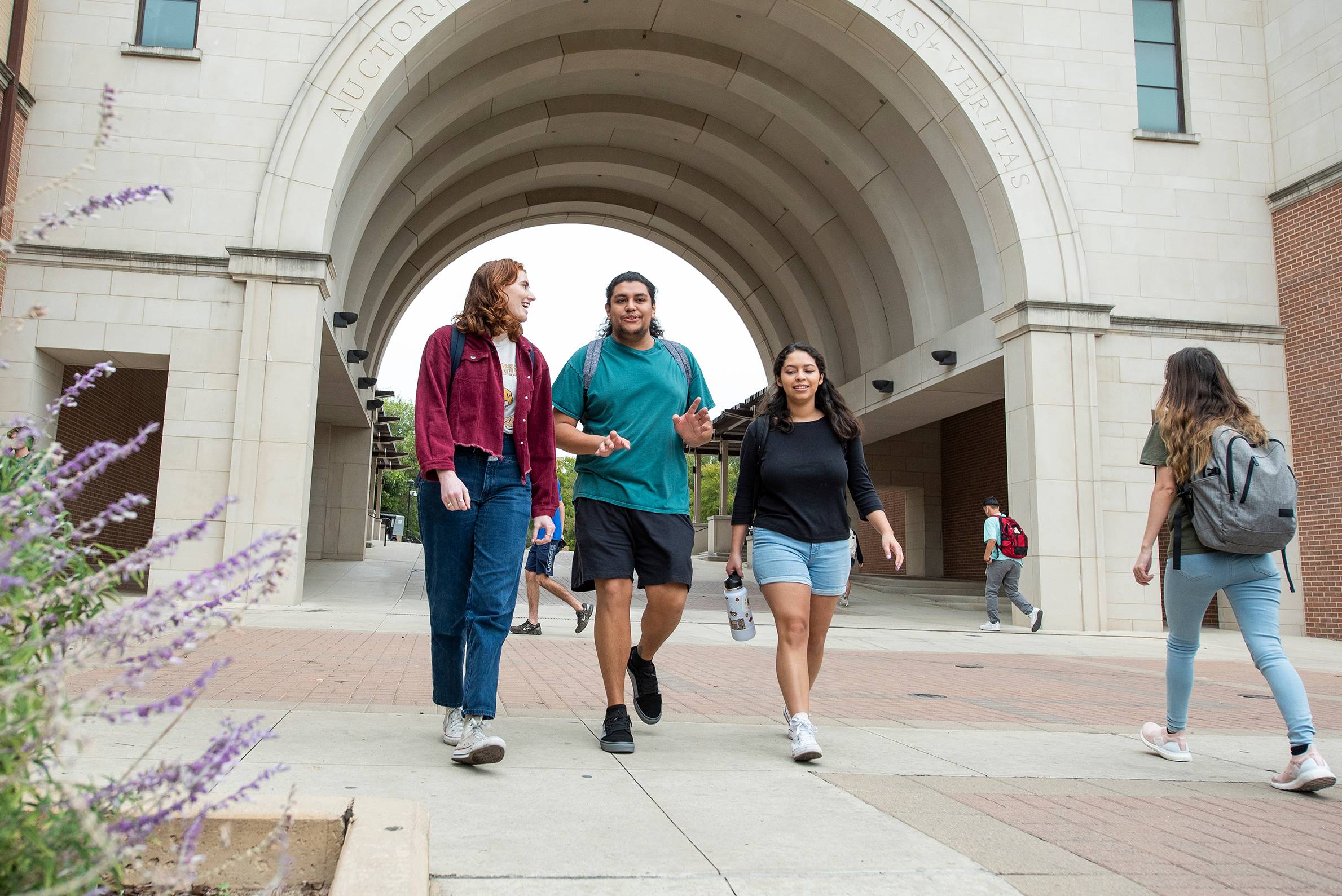 Three students talk and laugh while walking through campus.