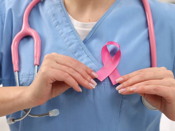 a medical professional holding a pink awareness ribbon up to their breast