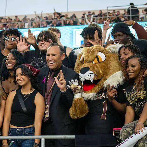 group of students posing with TXST president and Boko at a Bobcat sports event