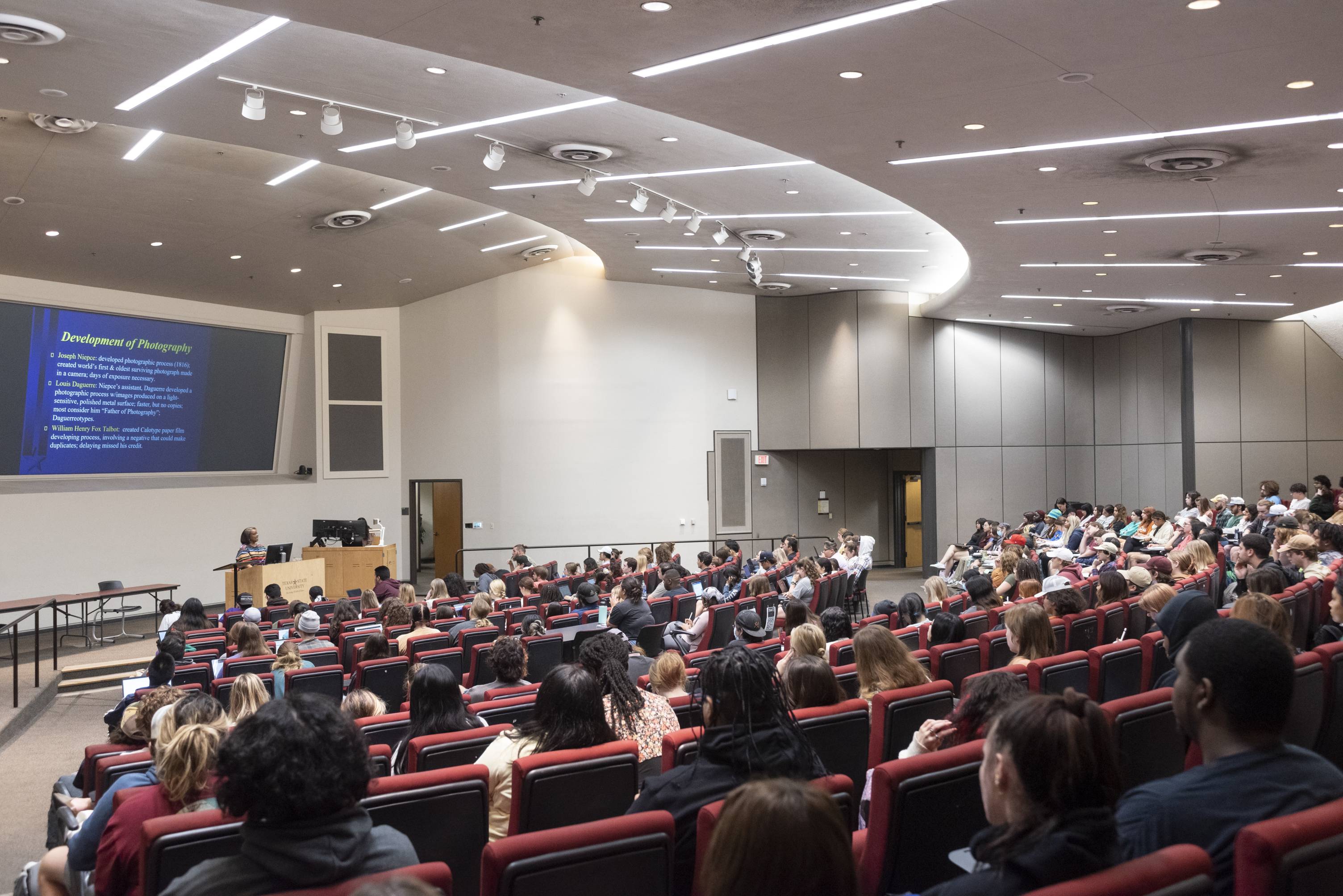 Students in a lecture hall intently watching a professor