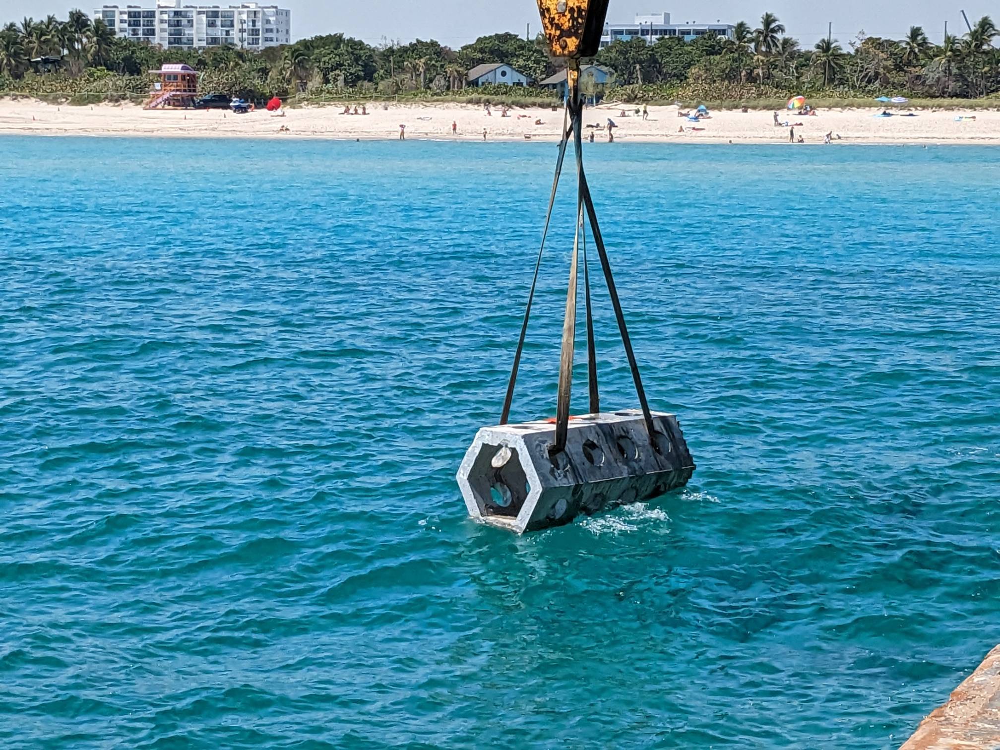 A massive hexagonal concrete tube called a 'seahive' being lowered into the ocean as part of a study on bridge scour.