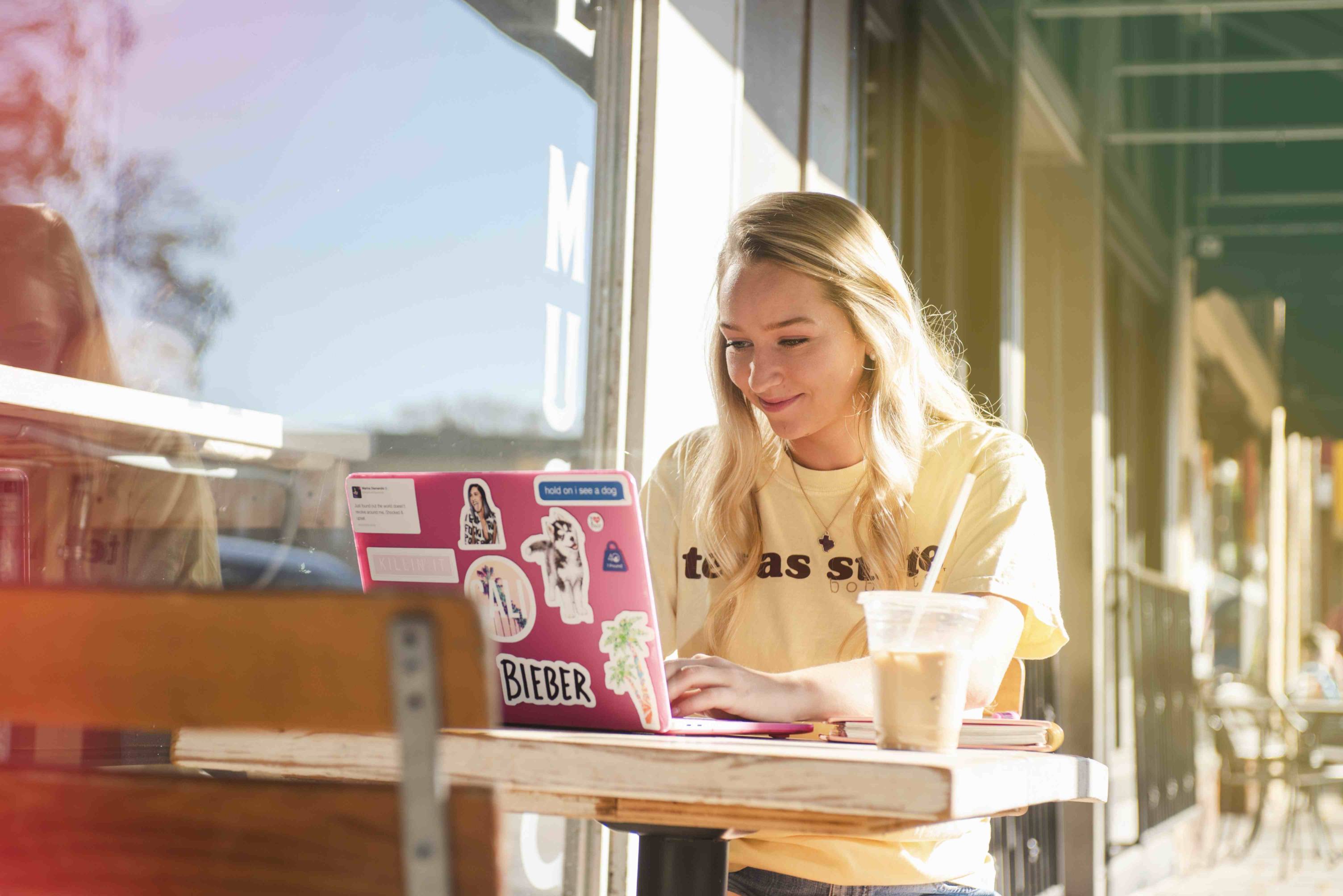 Girl works outside a cafe on a laptop covered in stickers