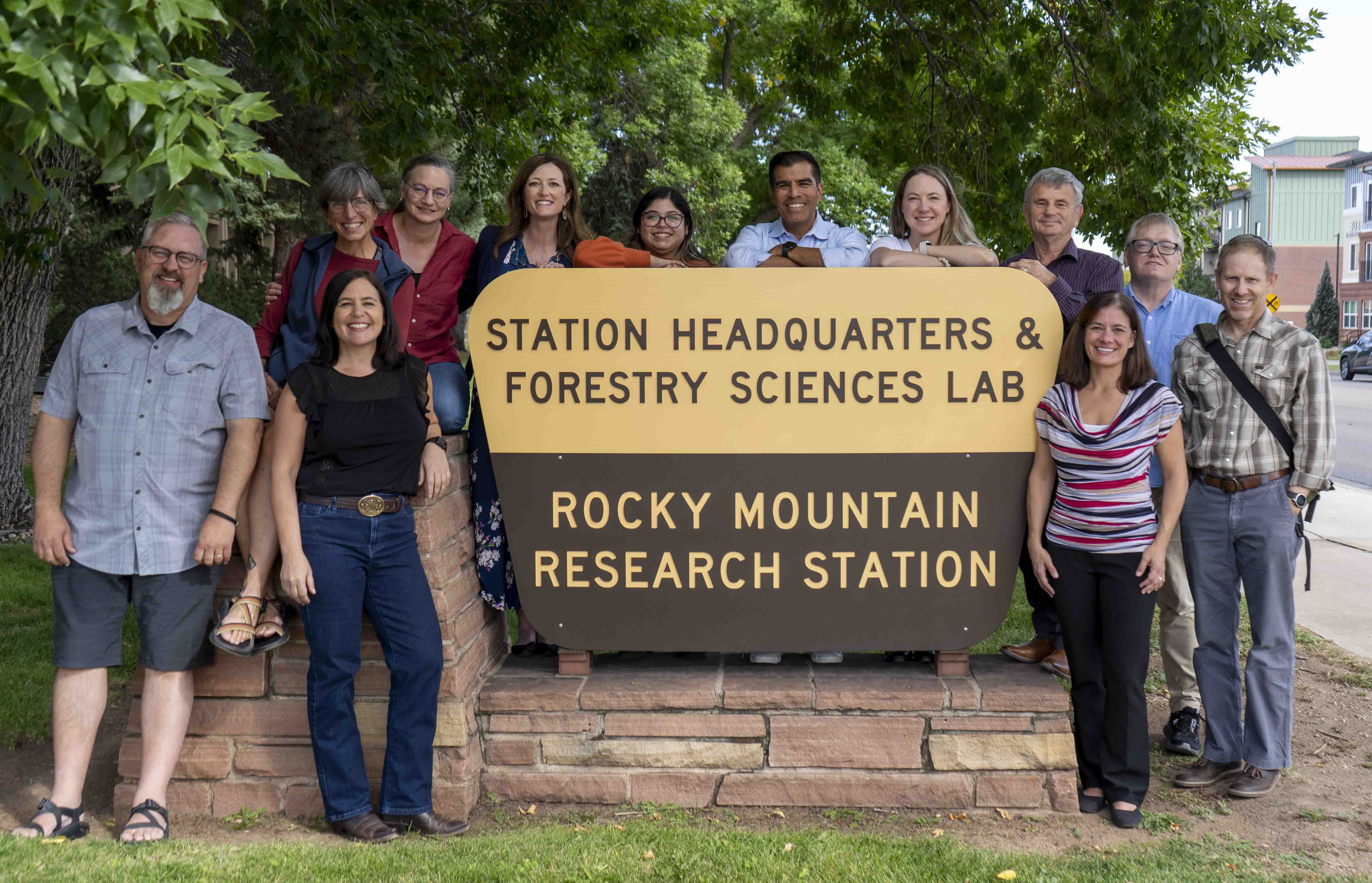 Gorup pf people smiling standing next to and behind at yellow and brown sigh that reads "station Headquarters & Forestry Sciences Lab Rocky mountain Research station"