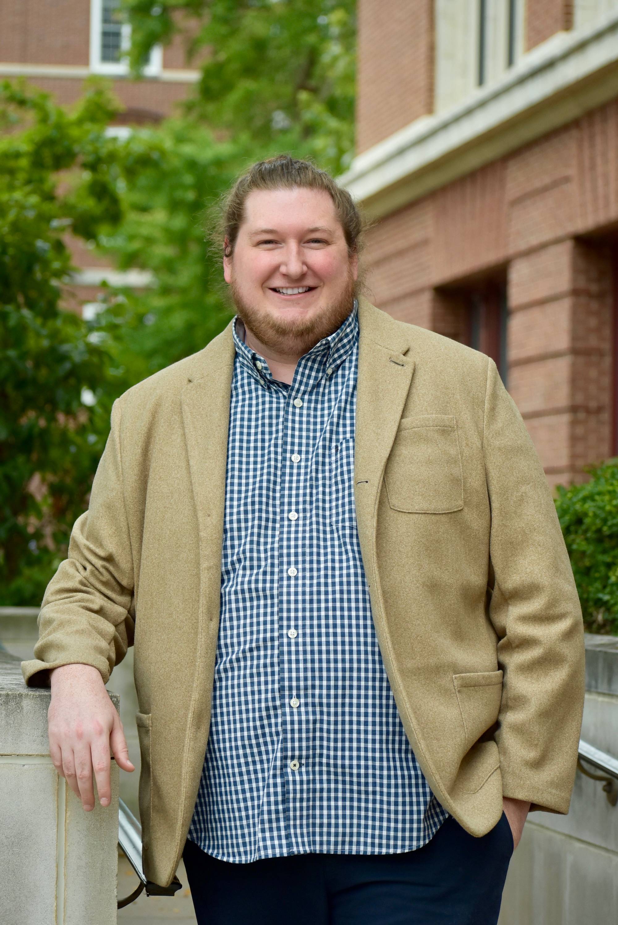 man iwth blue shirt and brown jacket standing smiling posing for photo