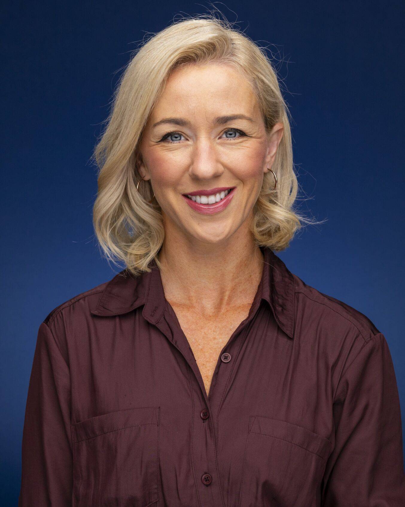 blonde women infront of blue backdrop smiling for photo