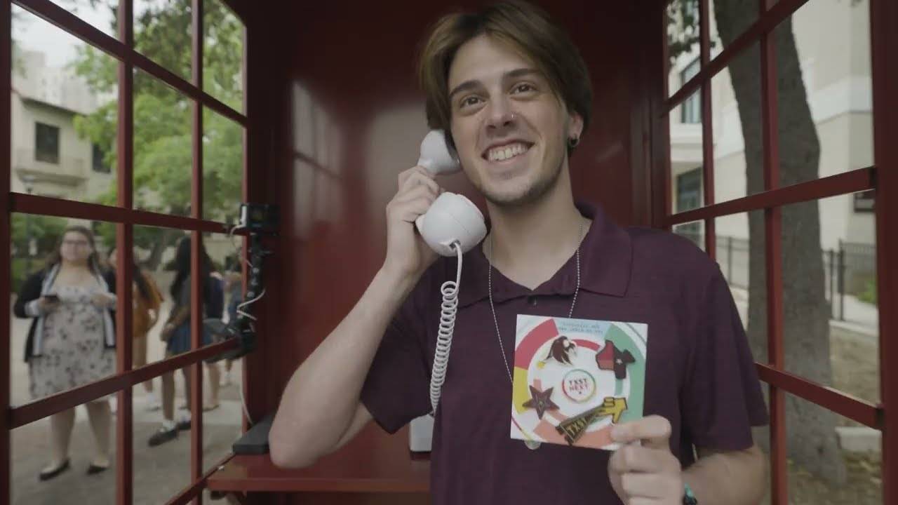 A student holding a corded phone in a phone booth holds up TXST merchandise while voiceovers of a students leaving messages about why they love TXST.
