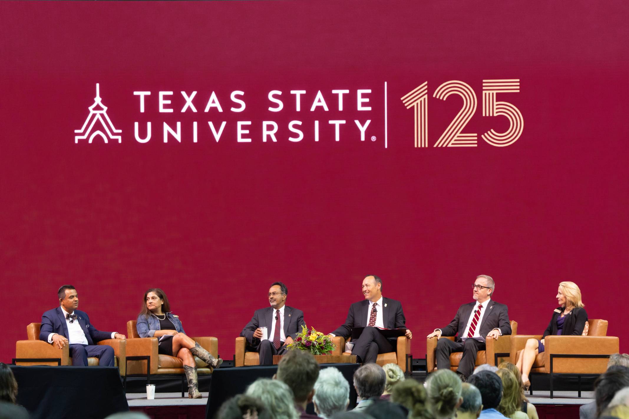 University president sits on a panel to discuss the state of Texas State; behind them, a maroon screen proclaims "Texas State University 125"