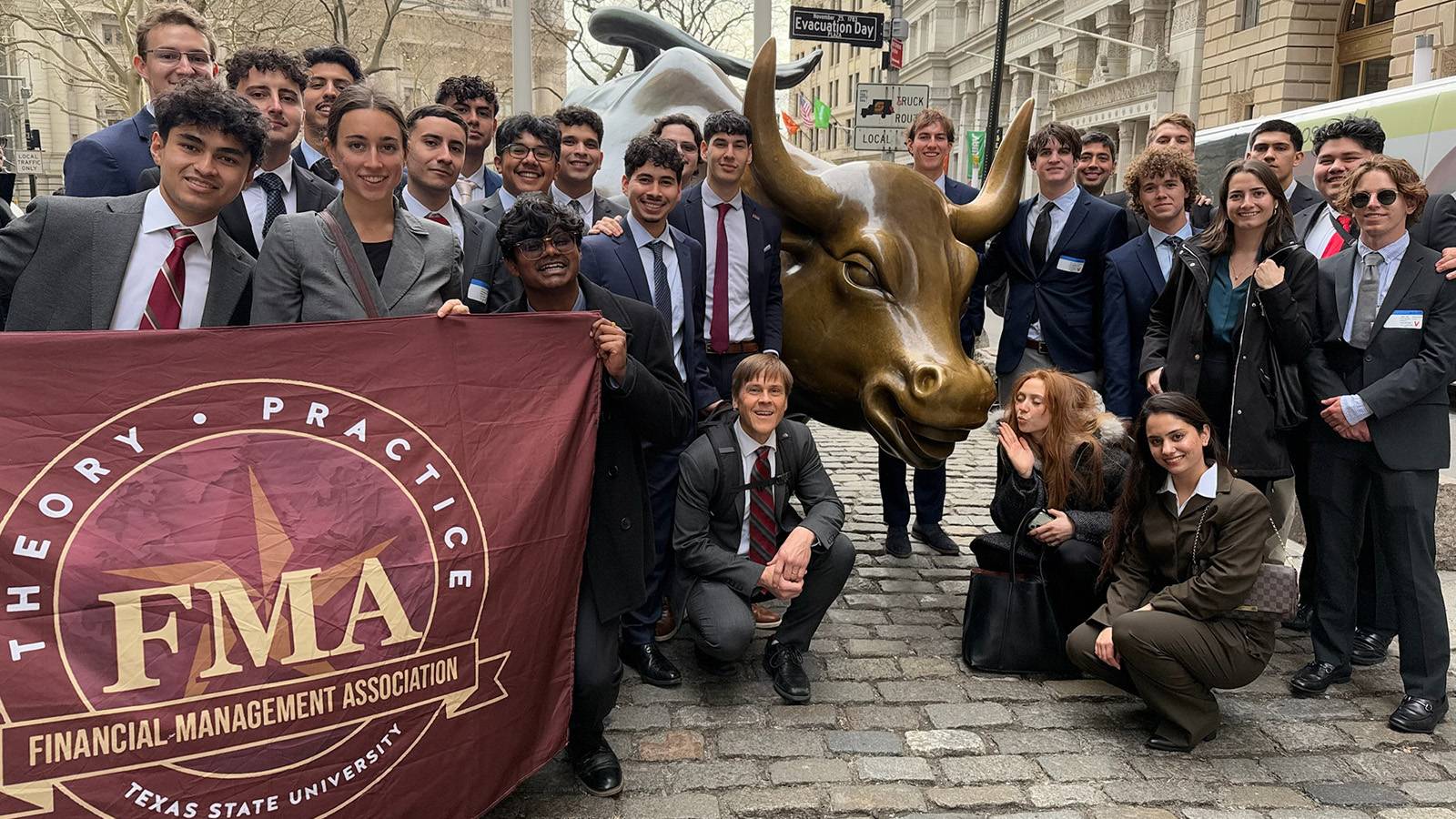 students dressed in business attire pose for photo in front of Charging Bull in New York City