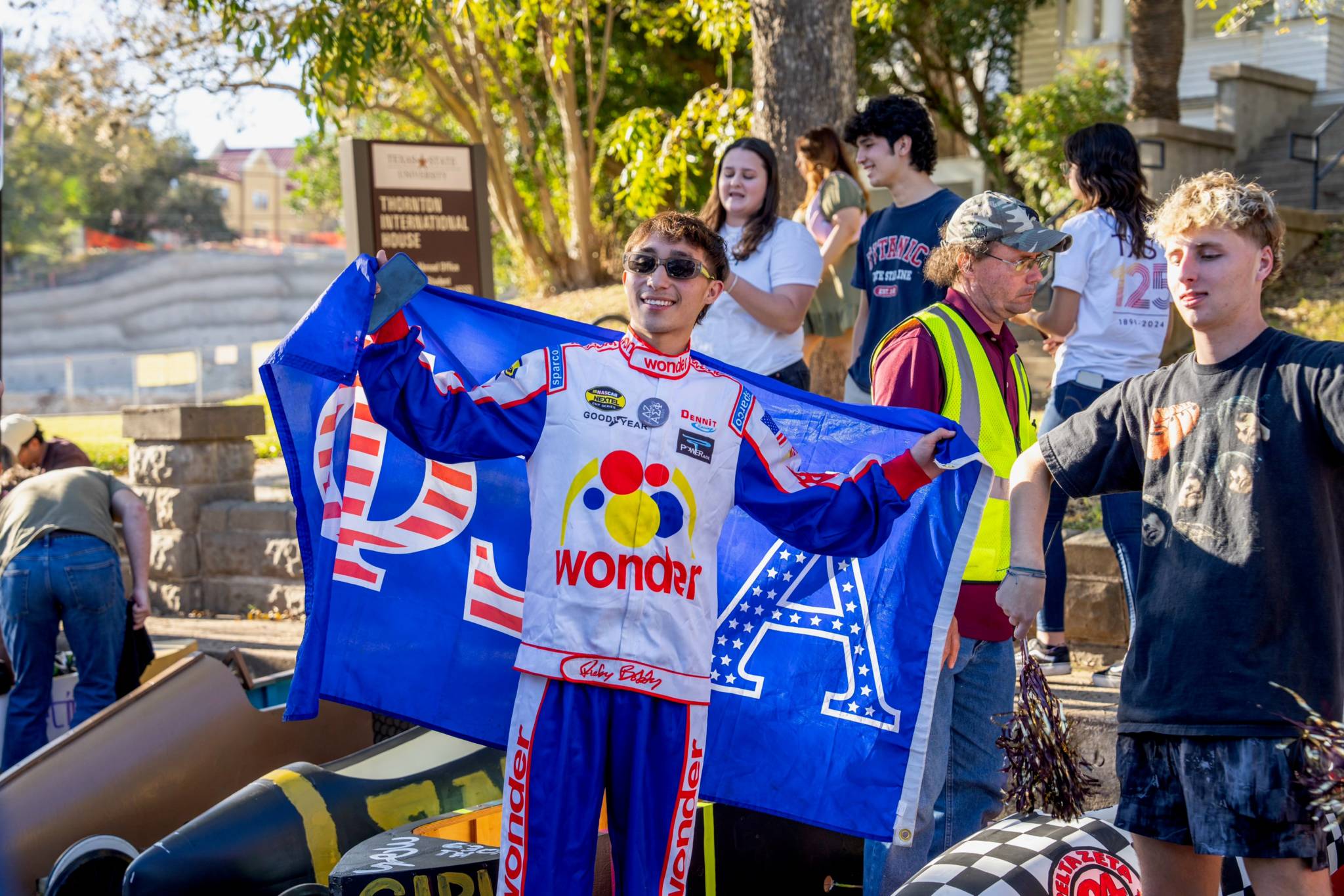 Student dressed in NASCAR body suit posing with fraternity flag