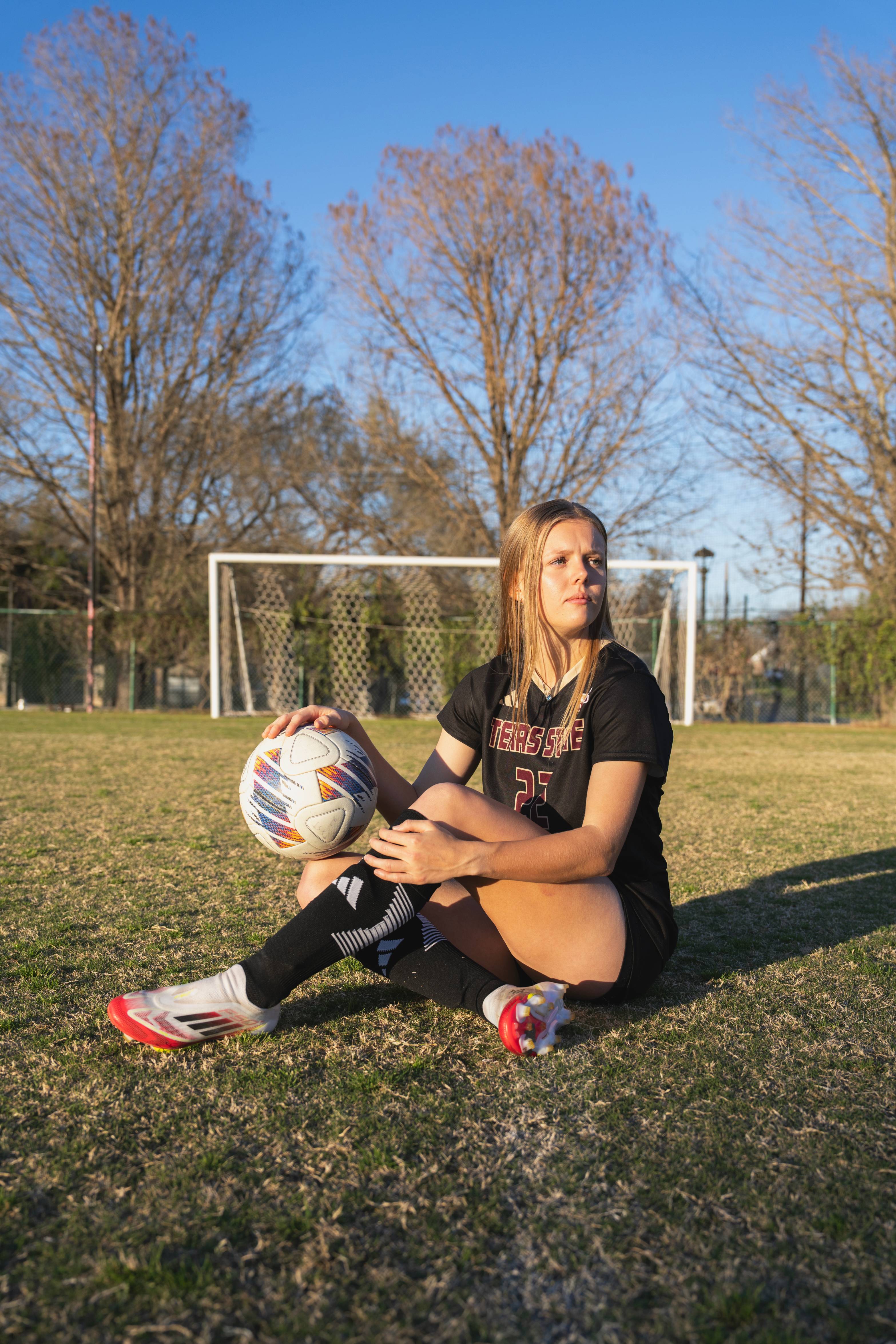 soccer athlete posing sitting down on the grass holding a soccer ball