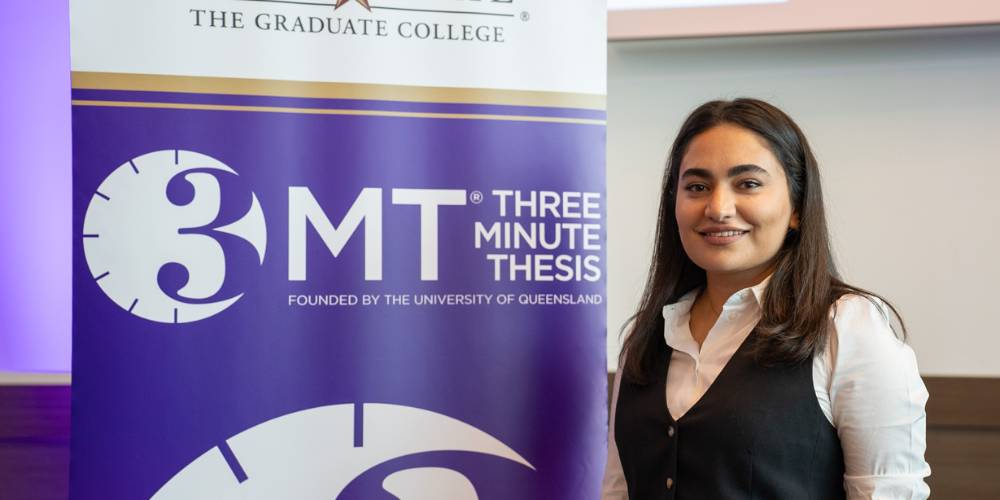 Anjumand Ashraf standing next to a 3MT sign holding her name tag and runner-up annoucement