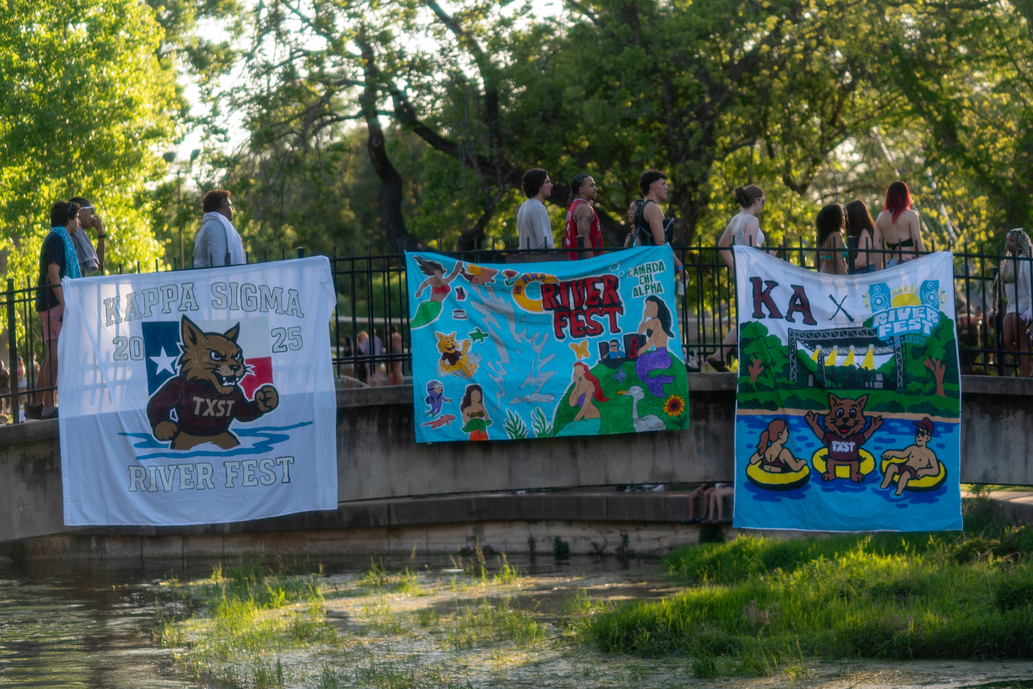3 painted banners hanging from a bridge at River Fest