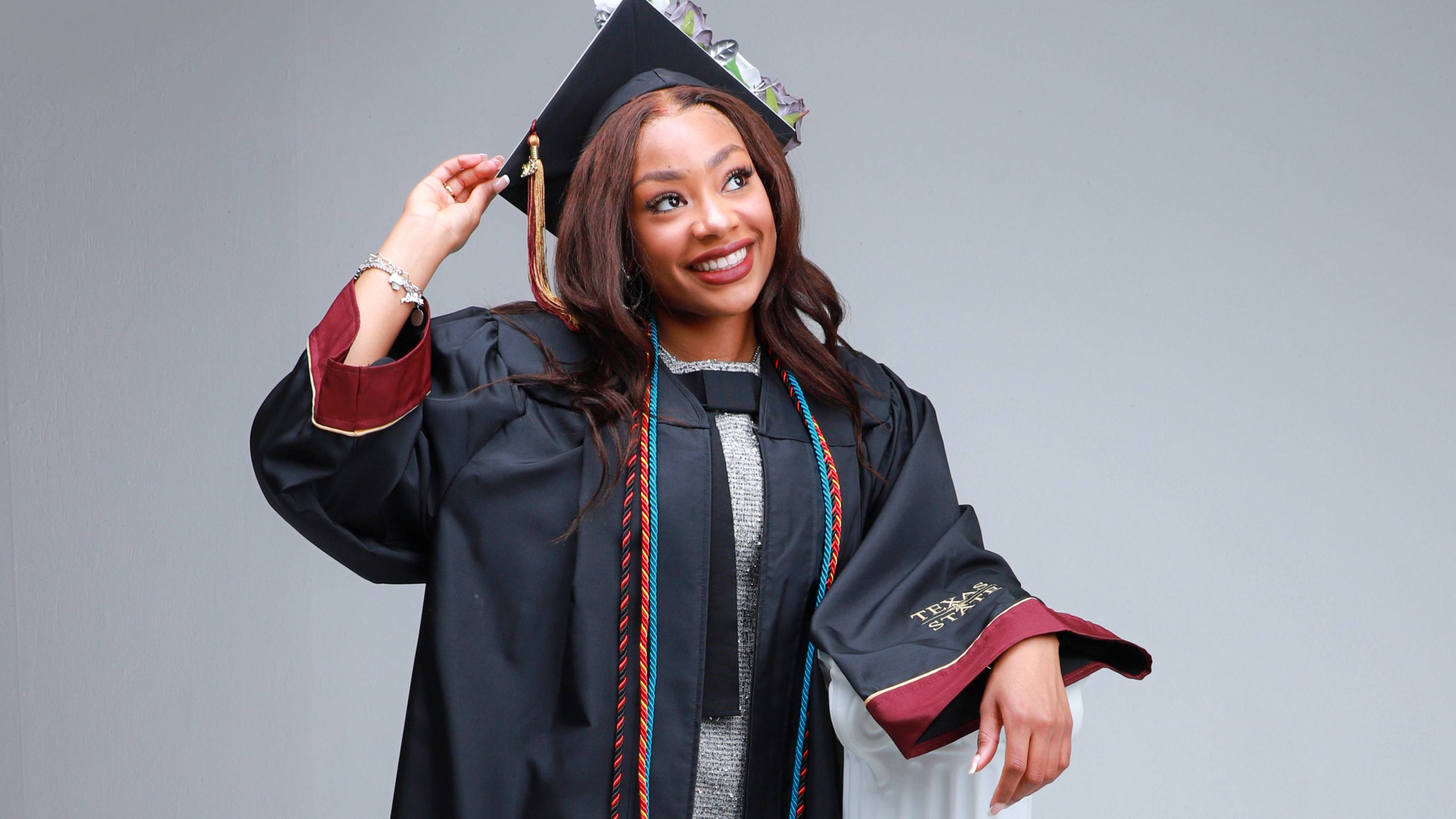 student wearing graduation gown and cap smiling and posing for a photo 