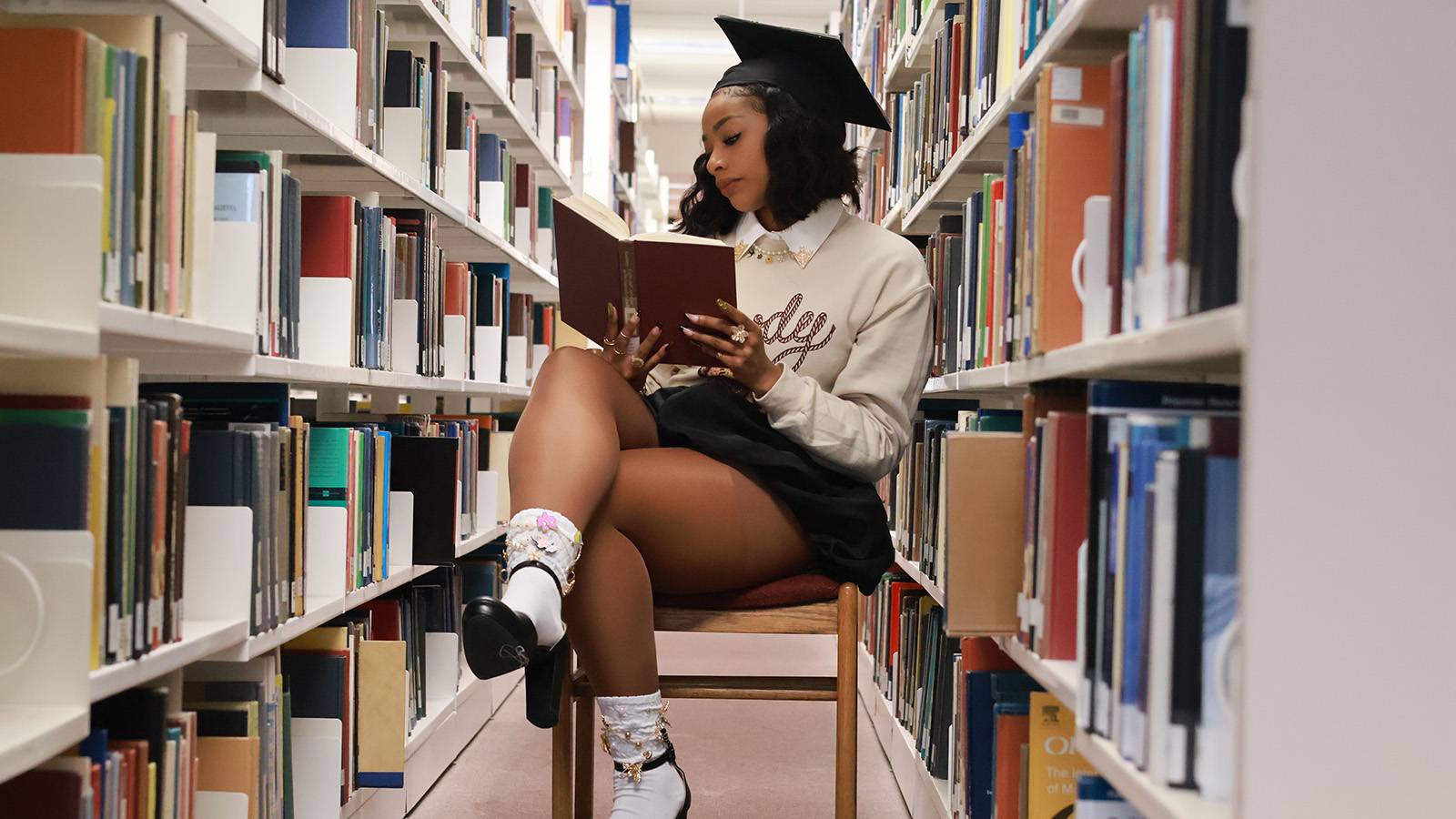 female student sitting in a chair in a library reading a book