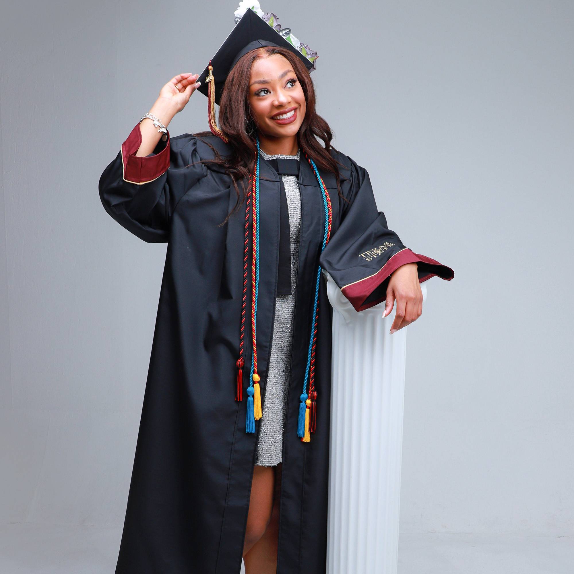 female student dressed in graduation cap and gown posing for photo and smiling