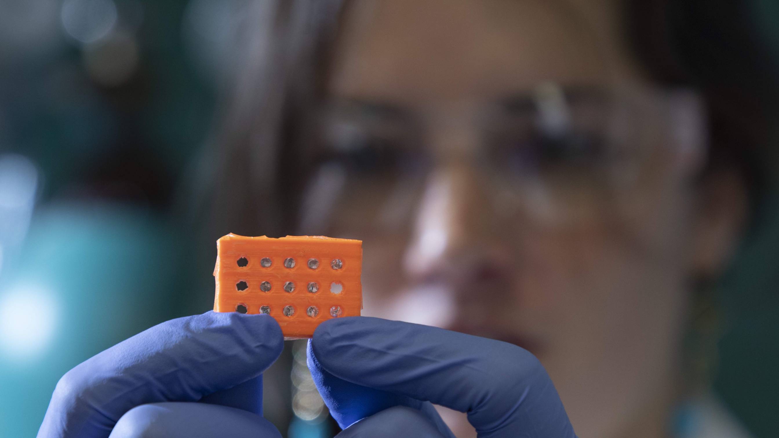 Woman in lab goggles holding an orange chip with rubber gloves