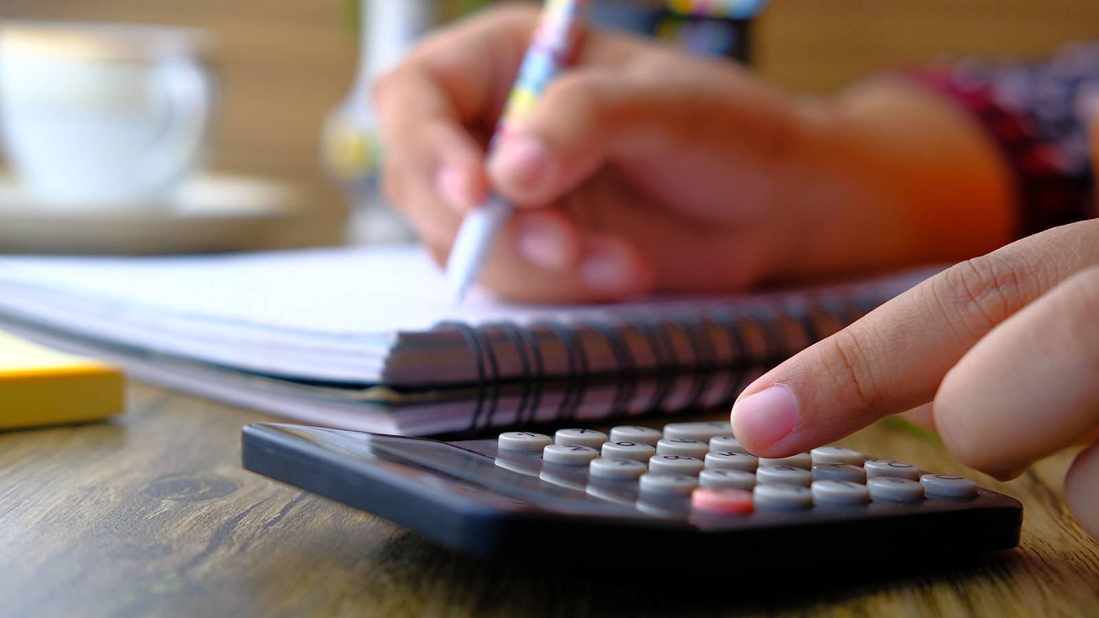 person working on calculator and writing on a notepad