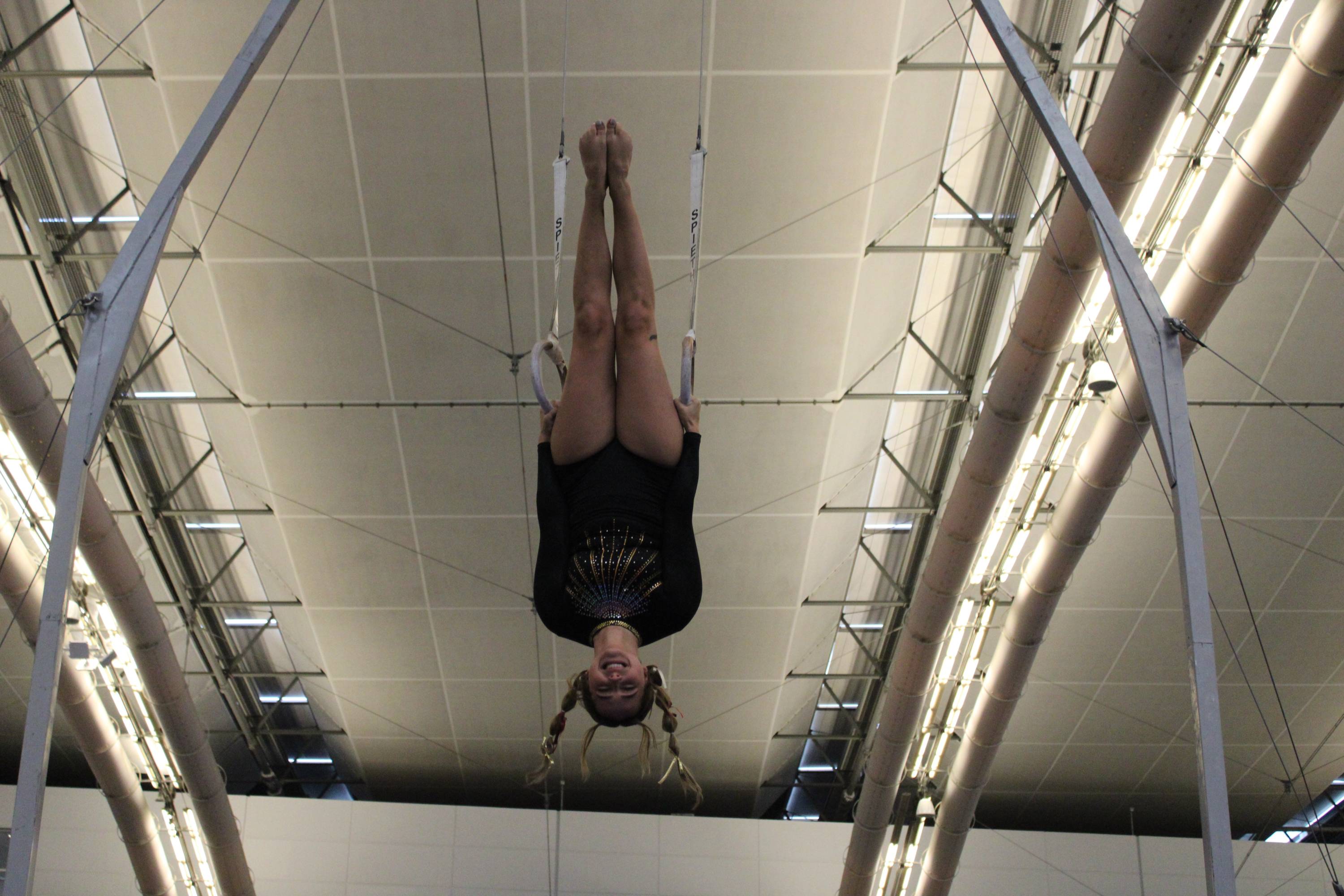 Gymnastics sport club member hangs upside down from rings while performing