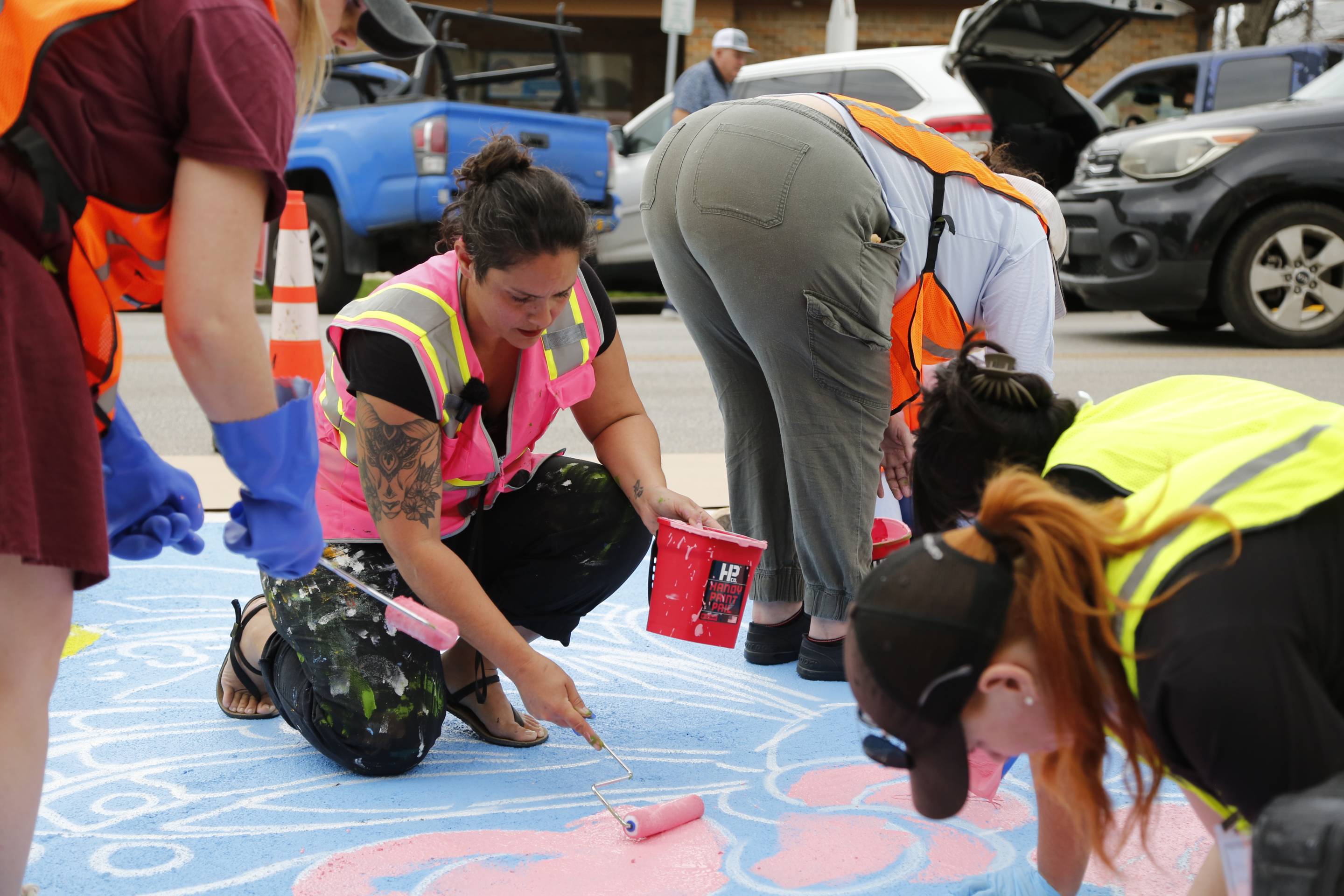 people in safety vests painting mural on street