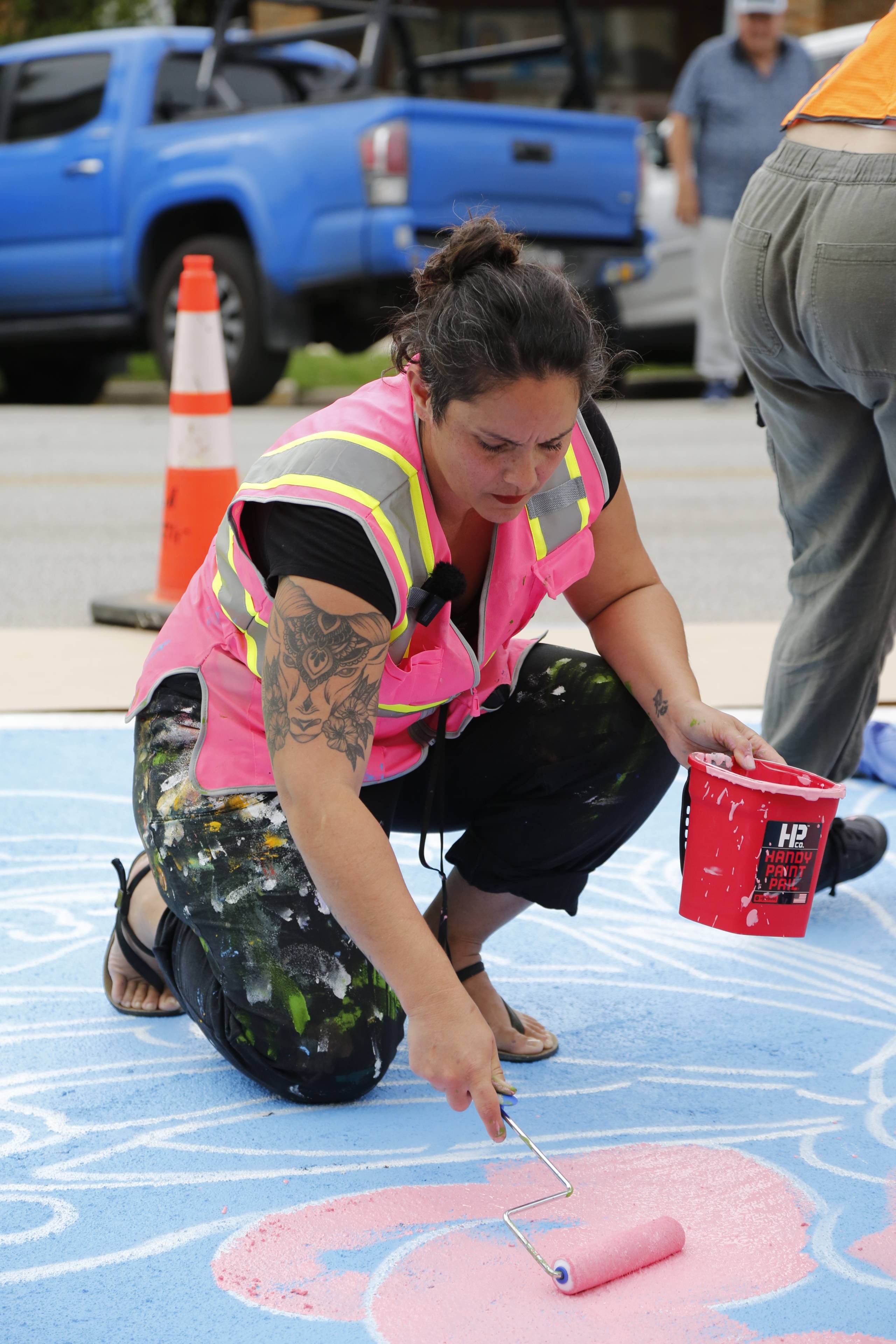 woman in pink safety vest uses a paint roller to paint mural on concrete
