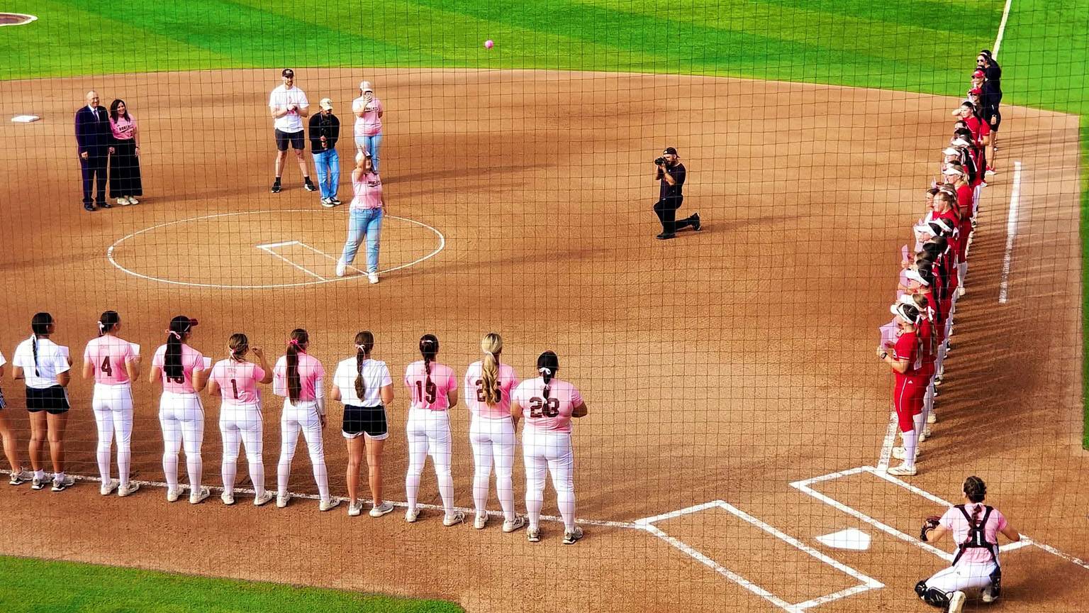 Kristen throws out the first pitch at a Bobcat softball game with players and the crowd watching.