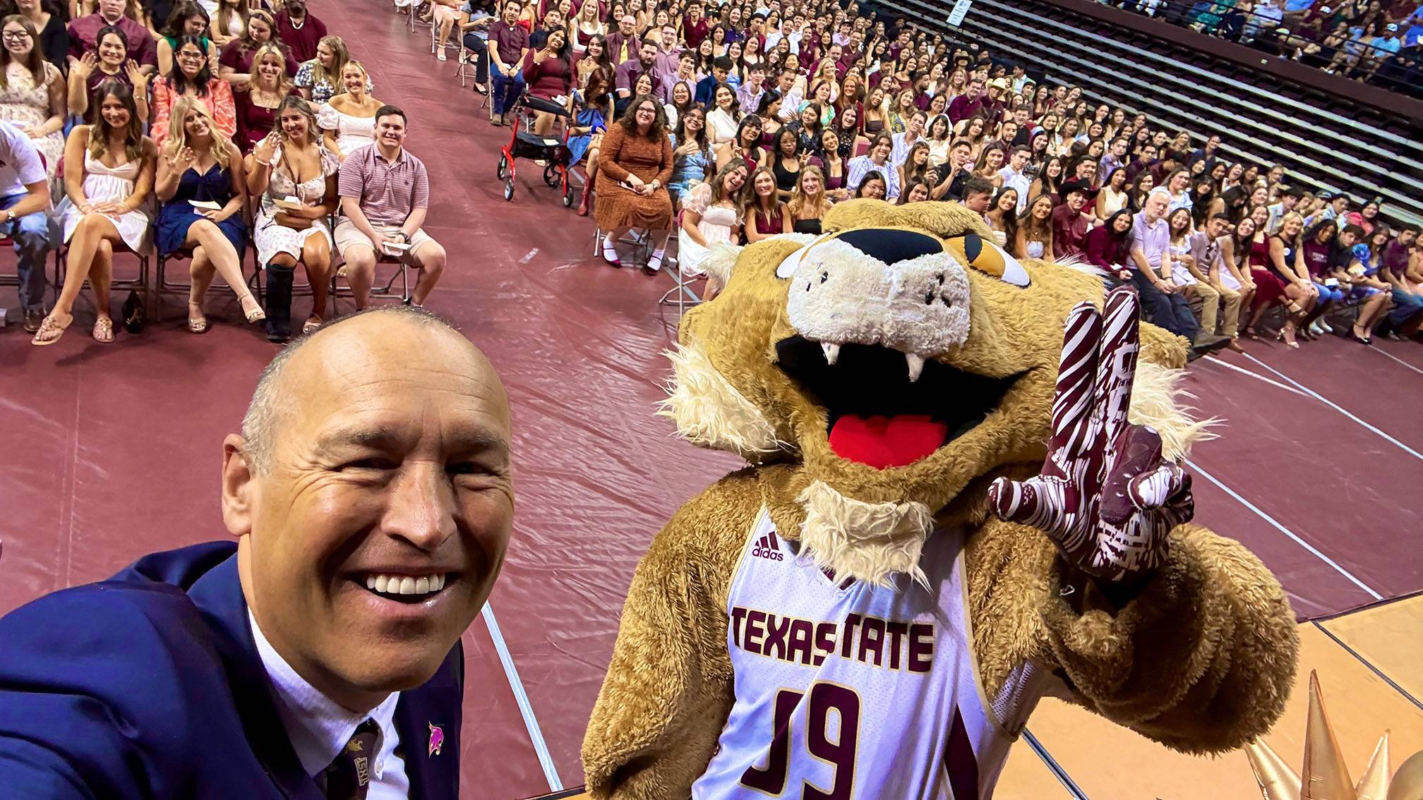 President Kelly Damphousse (left) takes a selfie with Boko and a crowd of graduating students.