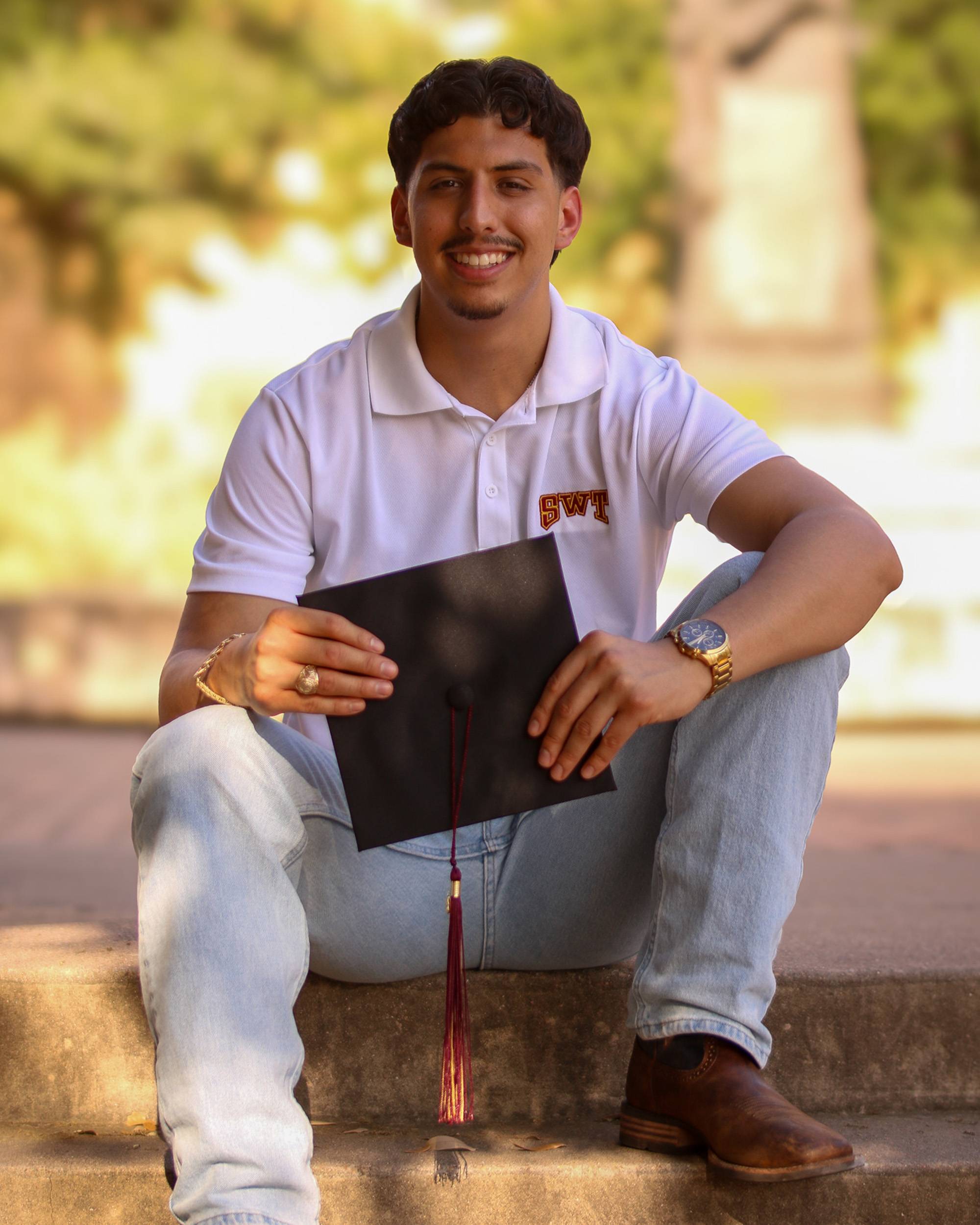 Young man sitting on steps holding graduation cap