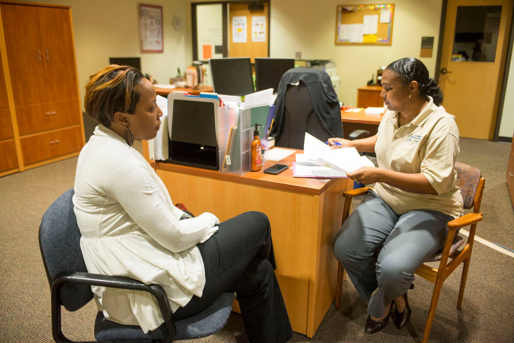 Woman sitting around desk talking. 