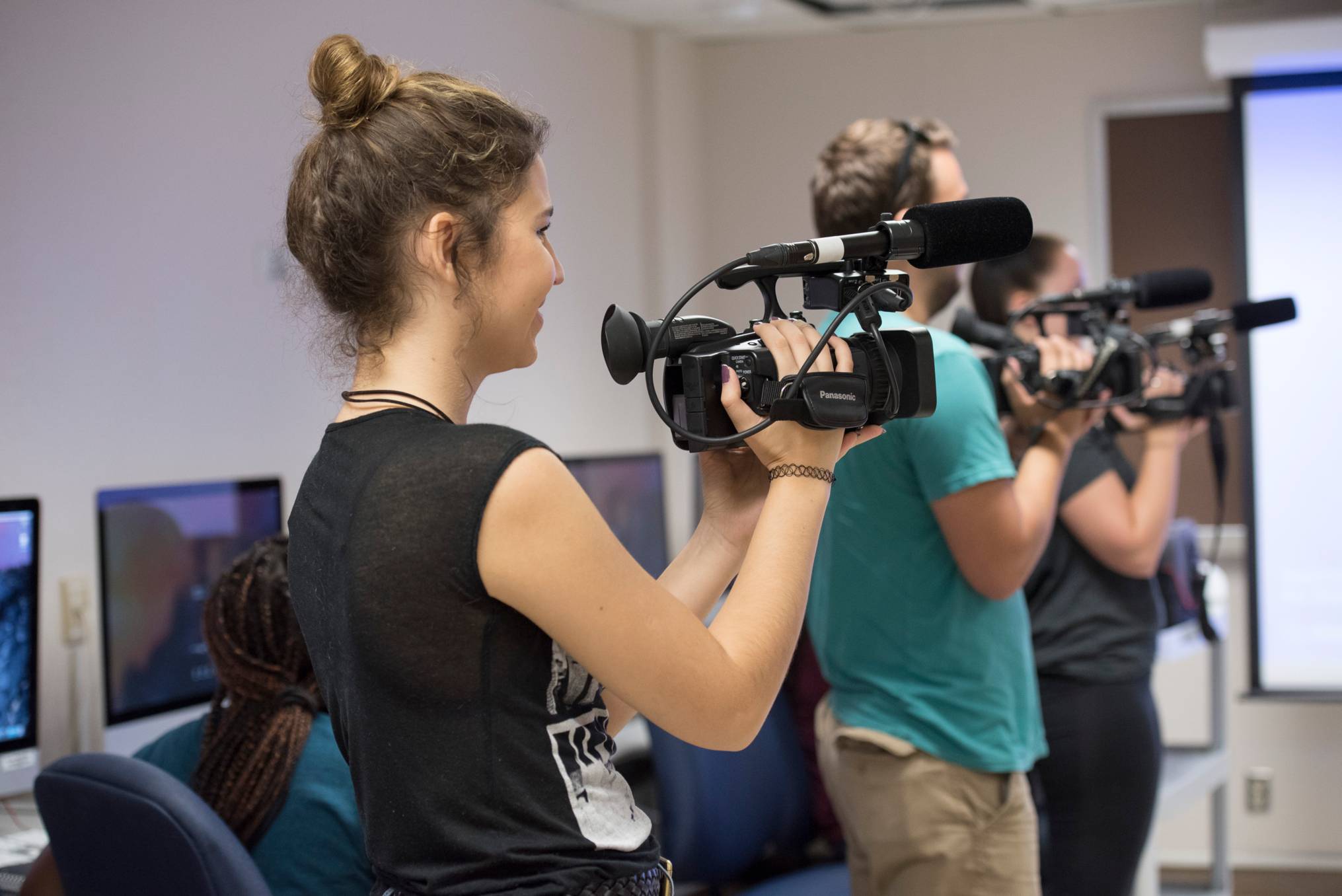 three standing students each holding camera equipment