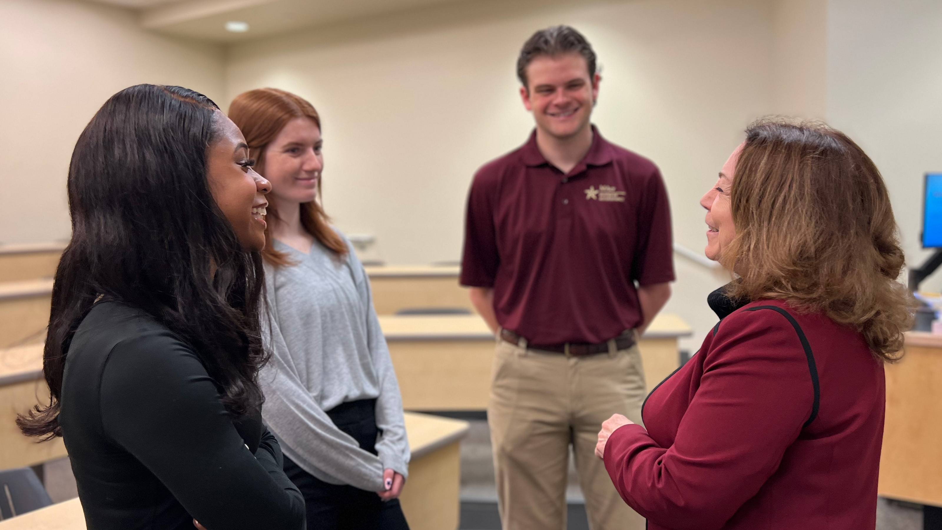 female professor speaks to three students in a classroom
