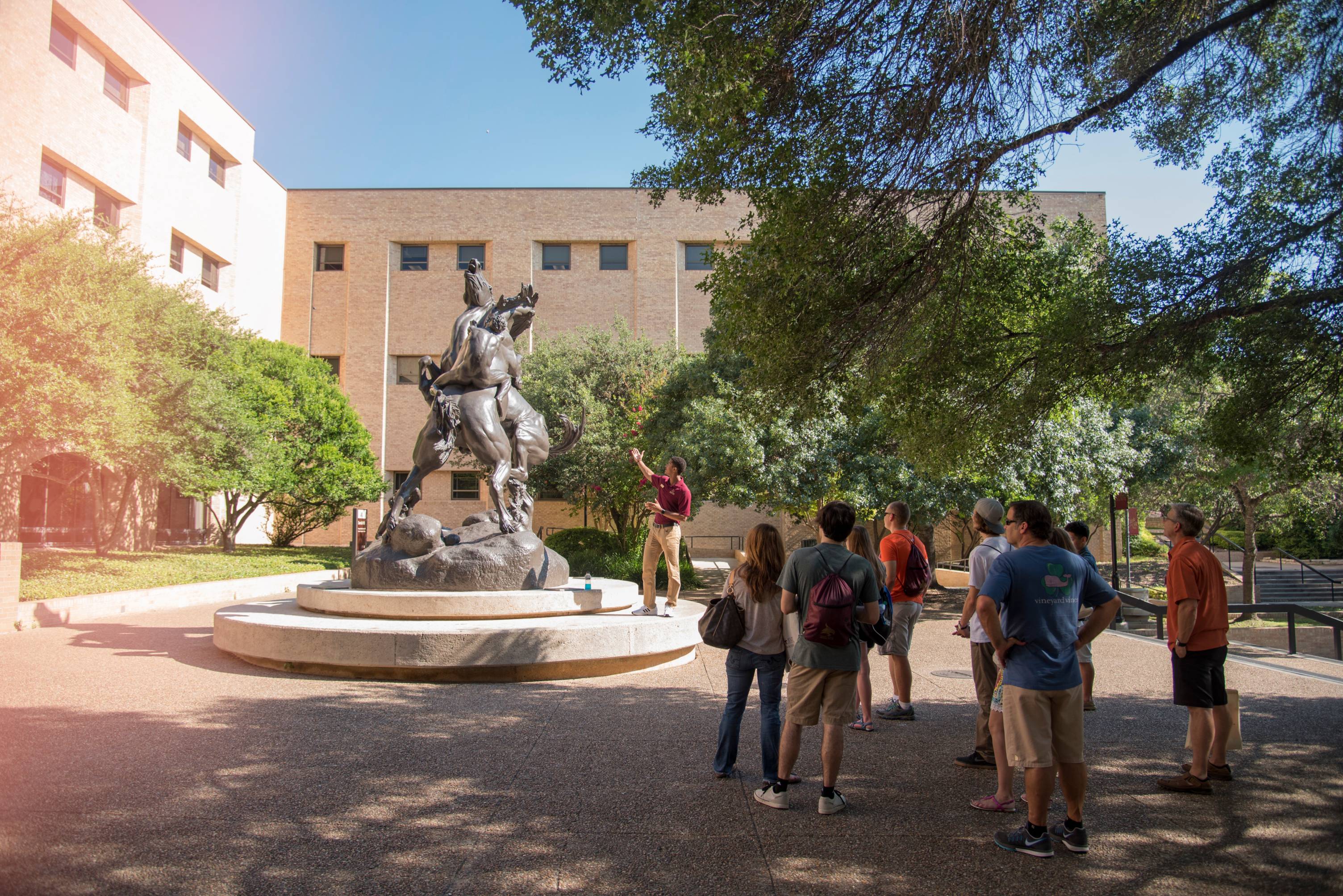 student speaking to group before a statue