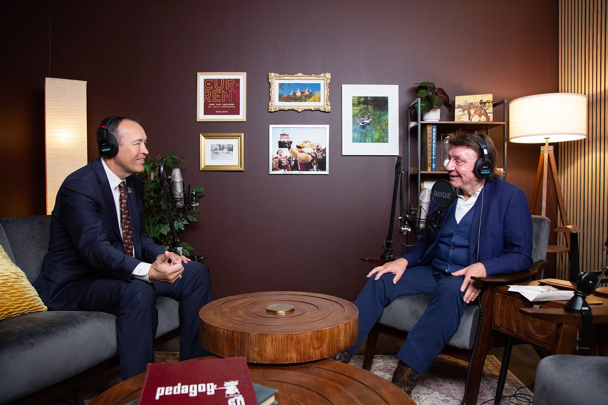 two men sit in podcast studio. they are wearing business attire and wearing headphones while speaking into microphones