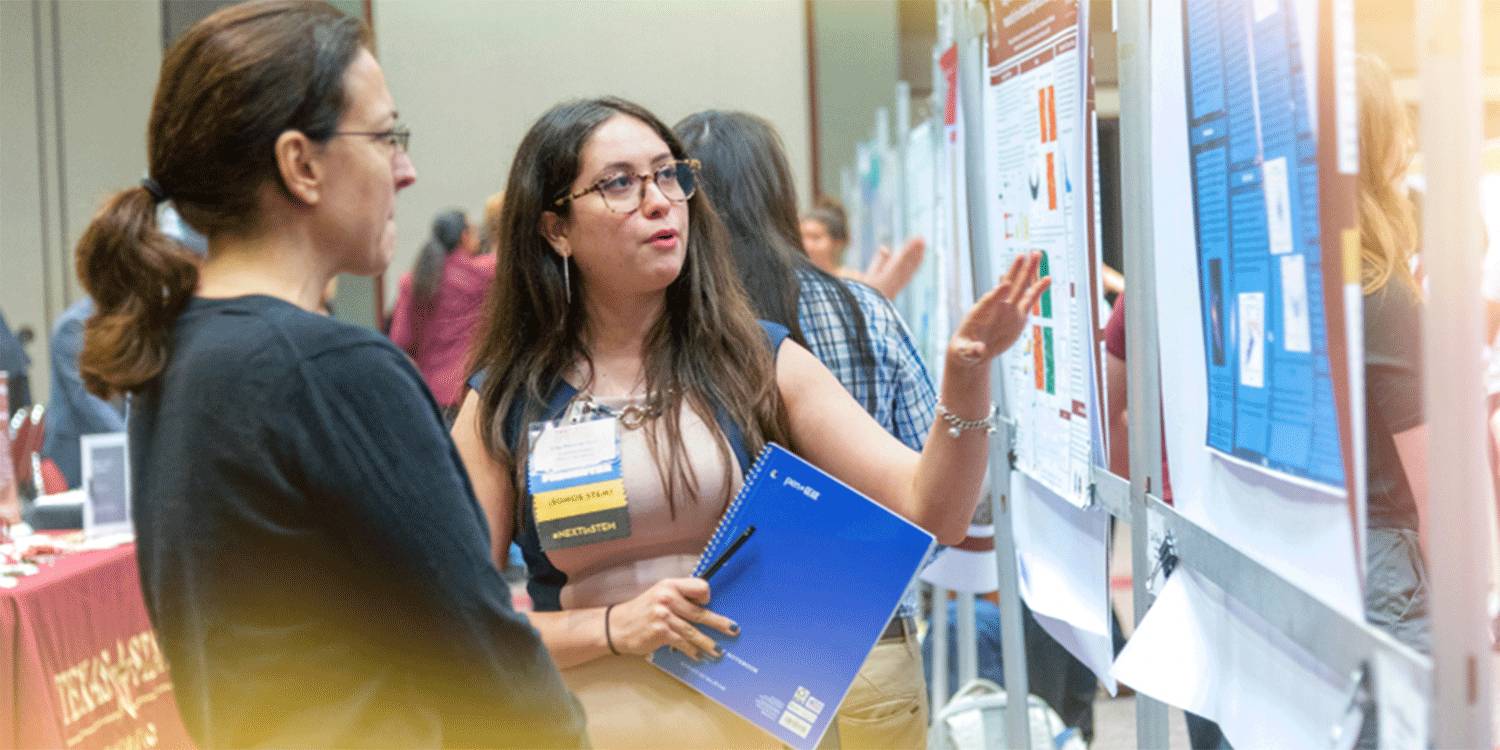 stduent explains research findings on a poster to an attendee of a research conference