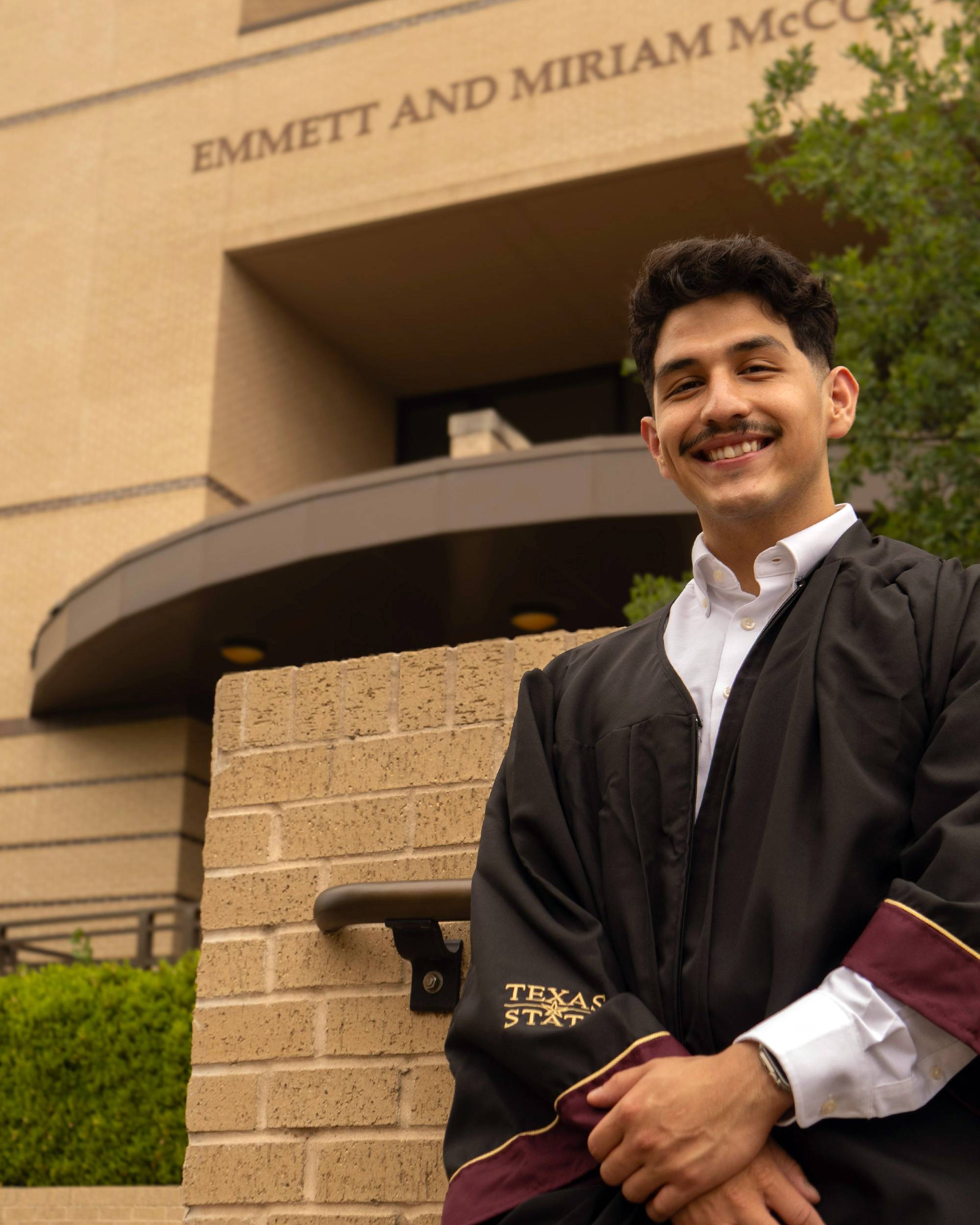Young man in graduation regalia posing outside McCoy Hall