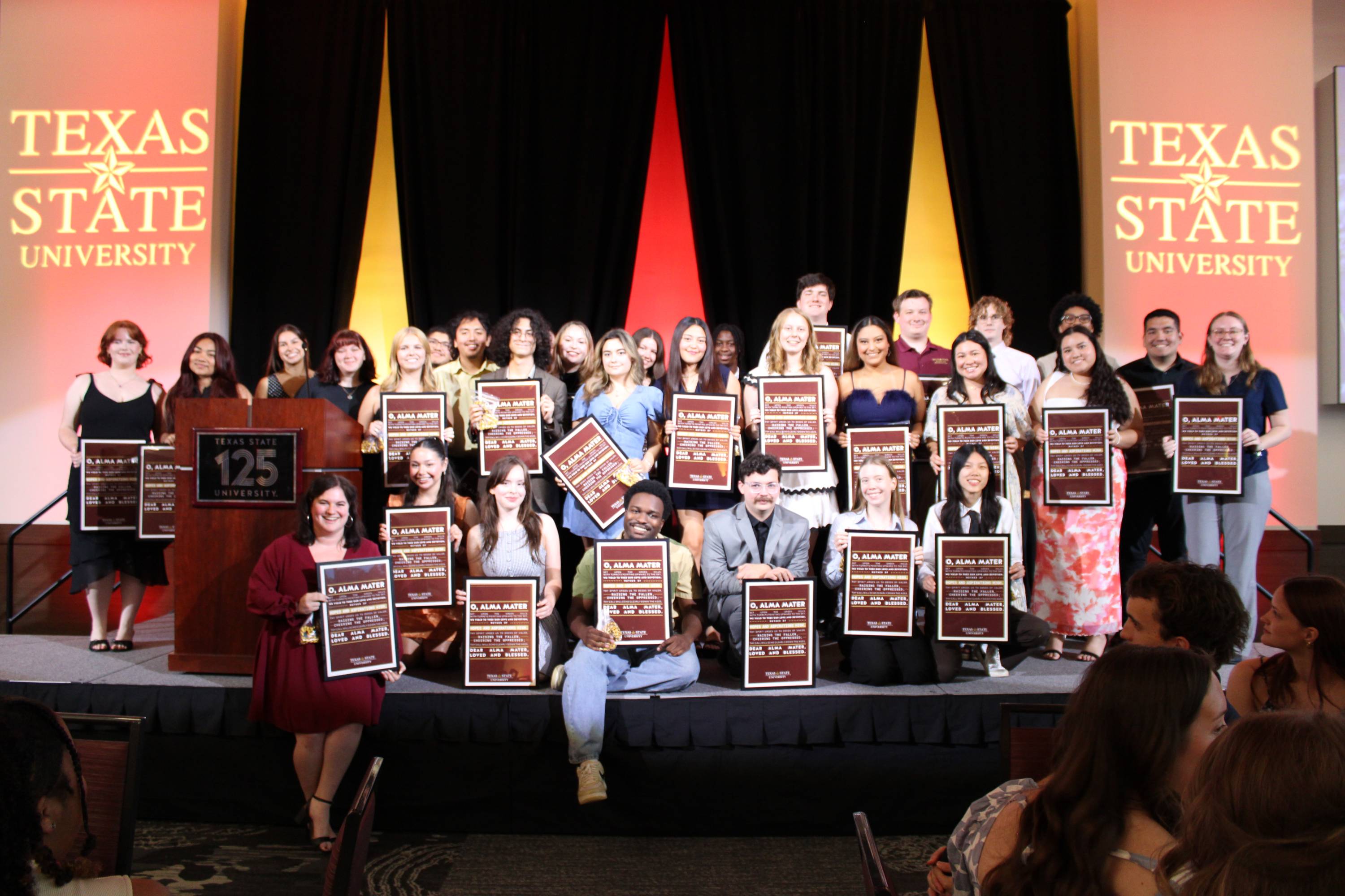 students holding a maroon poster on a stage