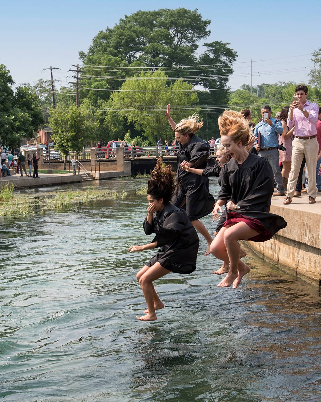 Three students jumping into the river after commencement
