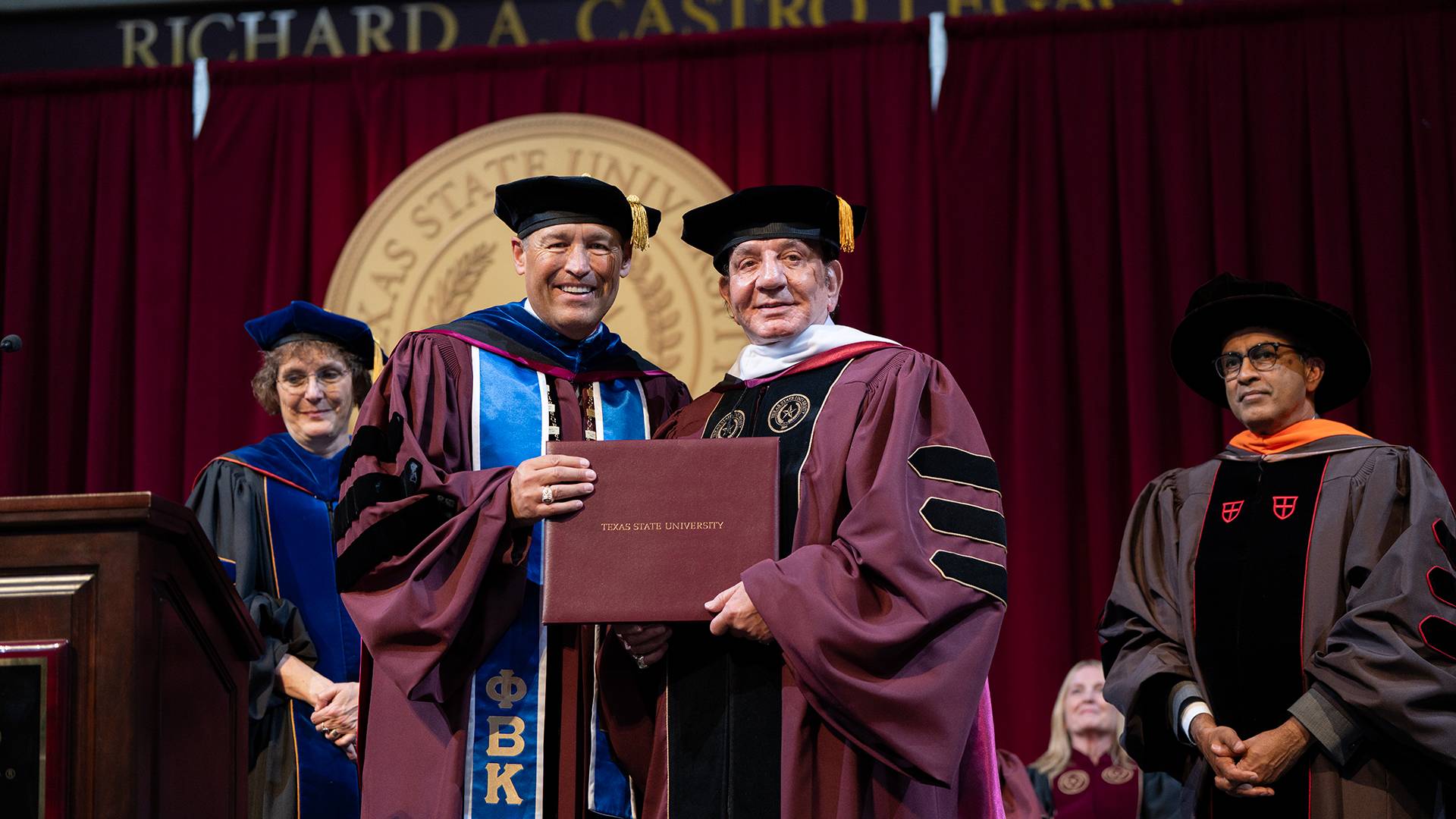 two people holding a diploma frame on a stage