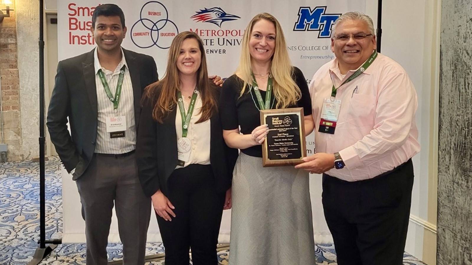 four graduate students posing for photo with award plaque